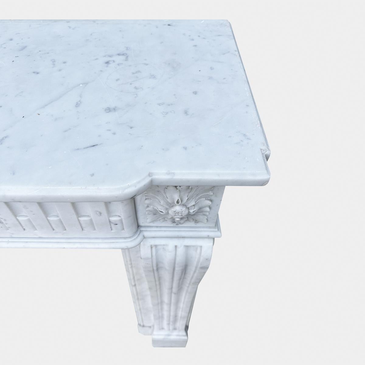 Ein kleiner antiker Kamin aus Carrara-Marmor aus dem 19. Jahrhundert im Stil von Louis XVI
Die Konsolenpfosten sind doppelt kanneliert und enden in klassischen quadratischen Patarae-Eckblöcken. Der Bogenfries ist mit Kanneluren versehen, darüber
