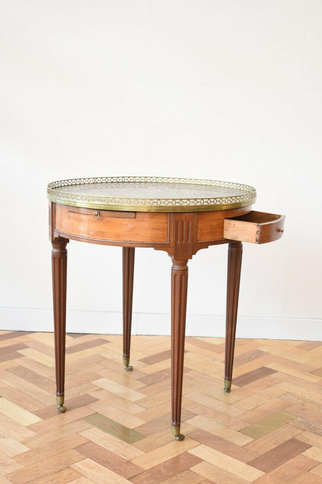 Lovely French mahogany bouillotte table dating back to the early 20th century.

This handsome piece features an inset circular marble top encased by a pierced brass gallery, ??two frieze drawers and leather pull-out trays. Its top is set on four