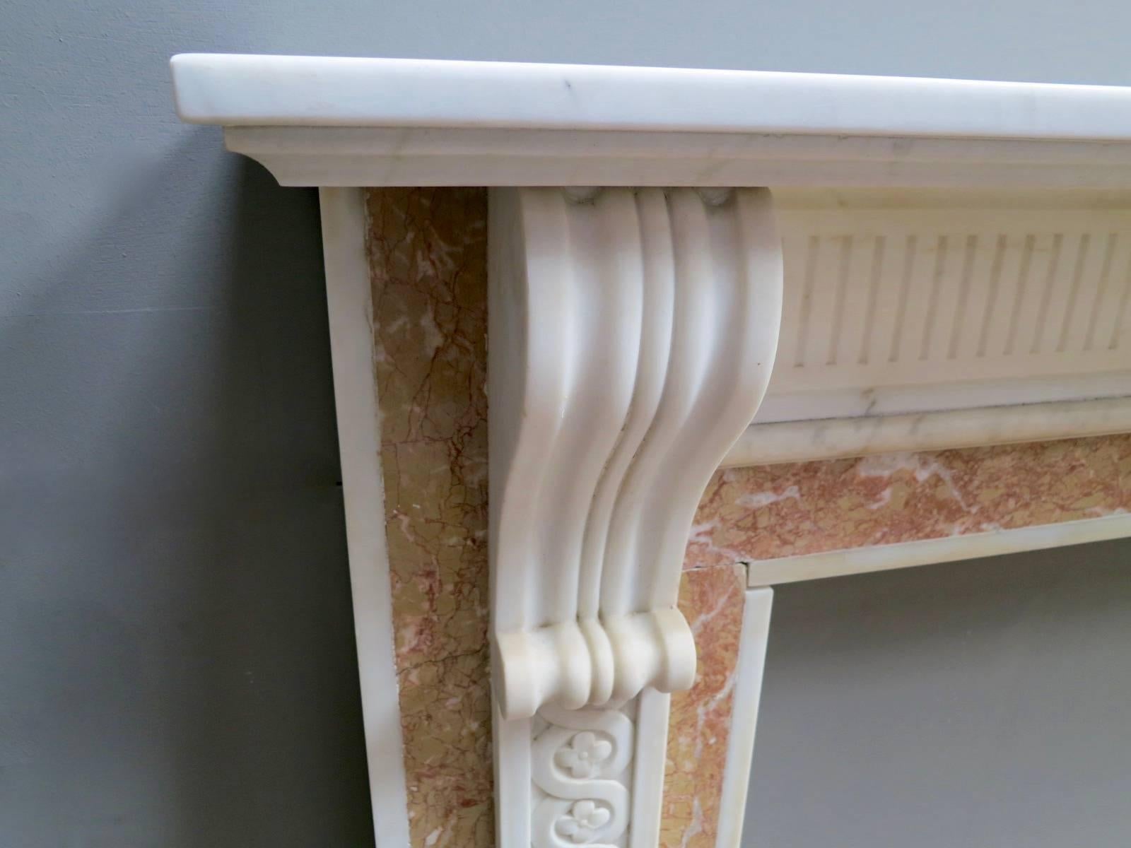 A late 19th century Georgian style fireplace in Statuary white marble and Brignoles marbles. The jambs with carved Guilloiche panels surmounted by carved corbel brackets, all in Statuary marble. The ingrounds and outgrounds in Brignoles. The stop