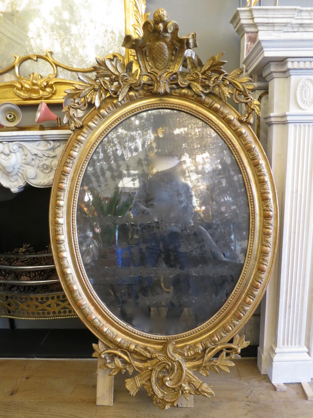 A late 19th century French gold gilt oval mirror with crested pediment flanked by tied laurel. The frame with egg and dart molding and inner beaded slip, with C-scroll, torch and quiver again flanked by tied laurel to bottom. The original plate