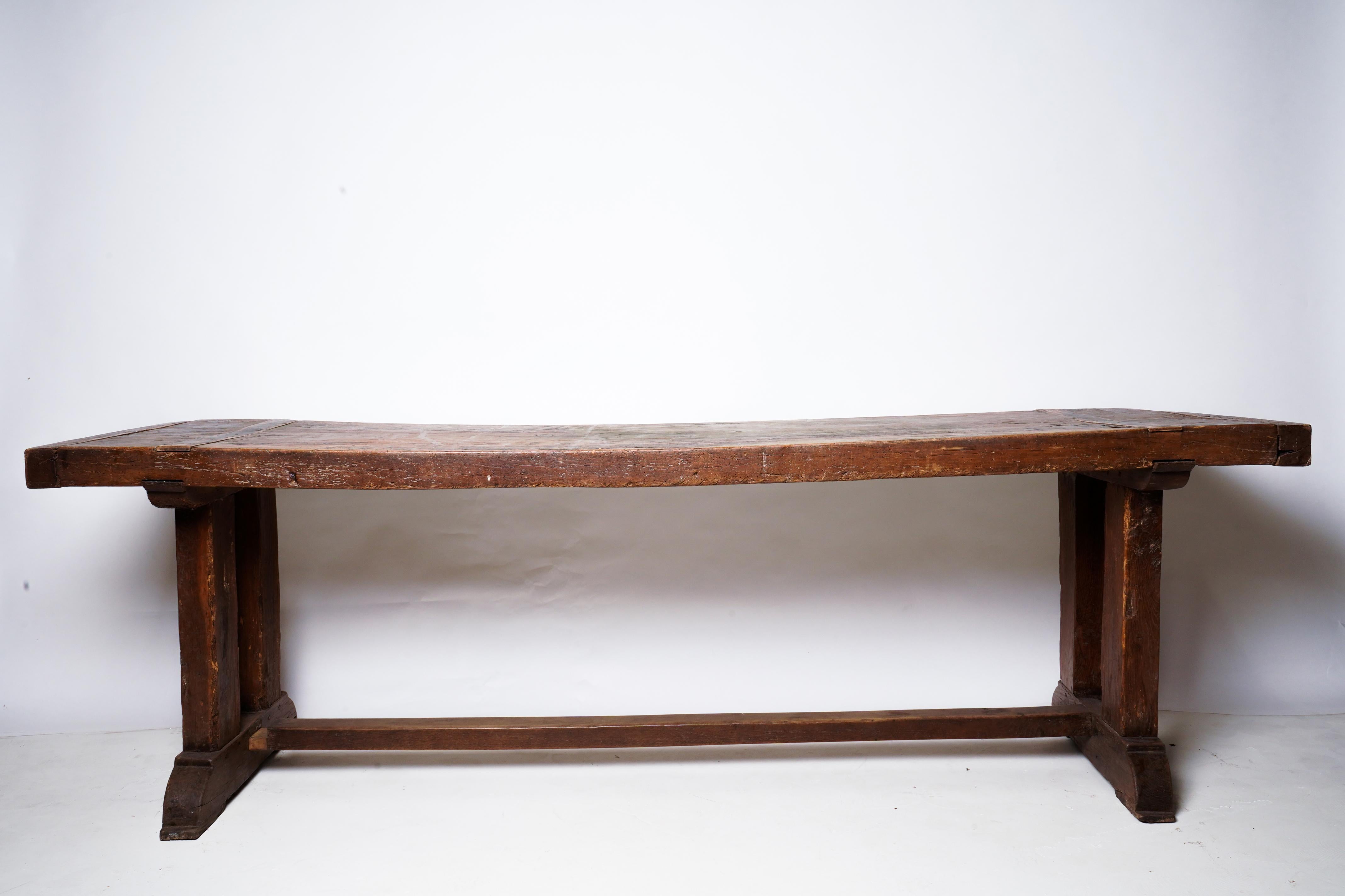 This extremely old table is made from a solid Walnut slab and retains its original trestle base. It's a very heavy and time-worn piece of wood with rich patina and a mysterious sag in its center. It can be refinished according to the customer's