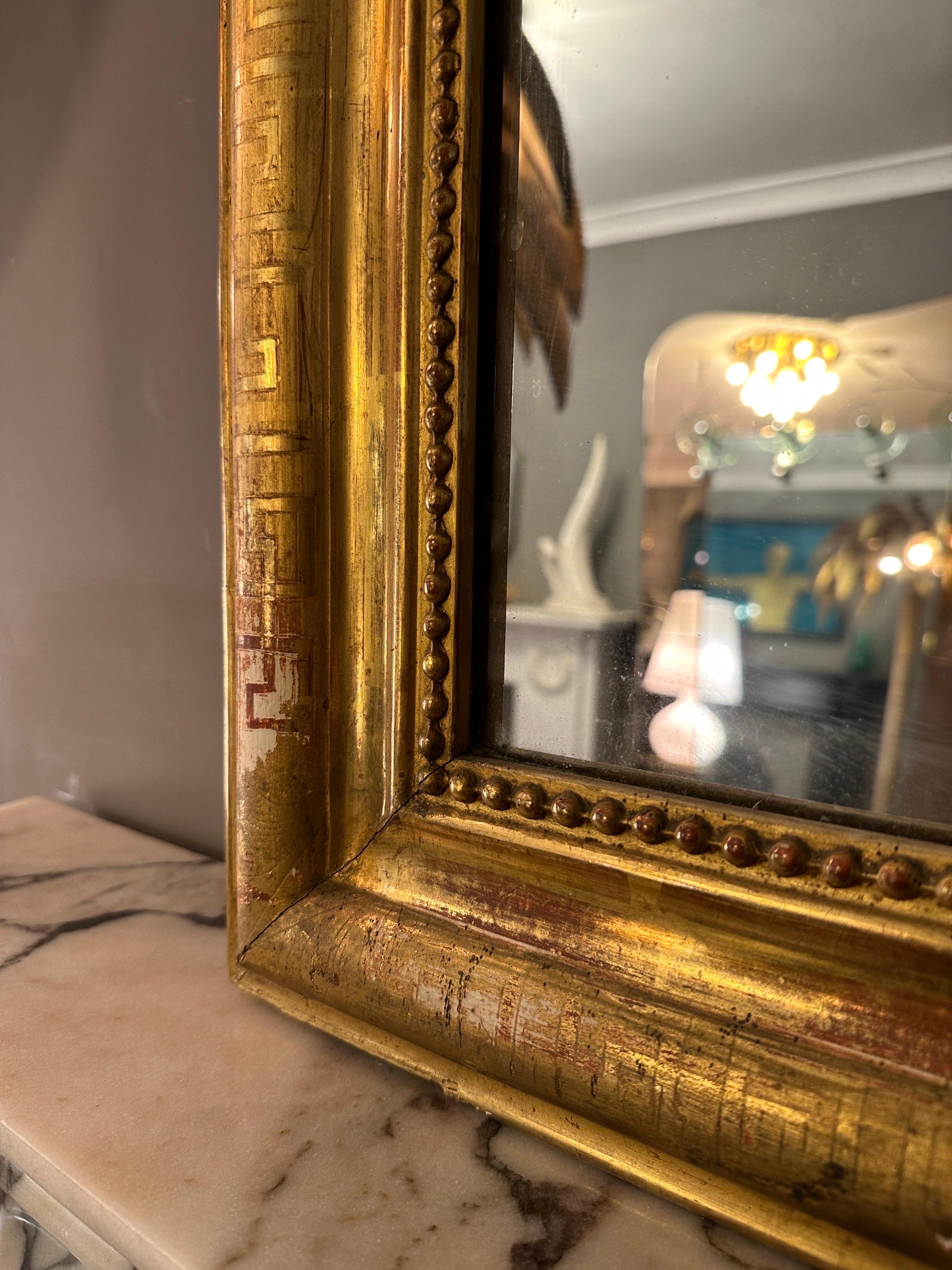 A gold gilt mirror from the late Louis Philippe period, with original glass plate, showing a little foxing in areas and a sparkle to glass. The frame with Greek key decoration and inner beaded slip. Gentle warm patina with areas of age related wear.