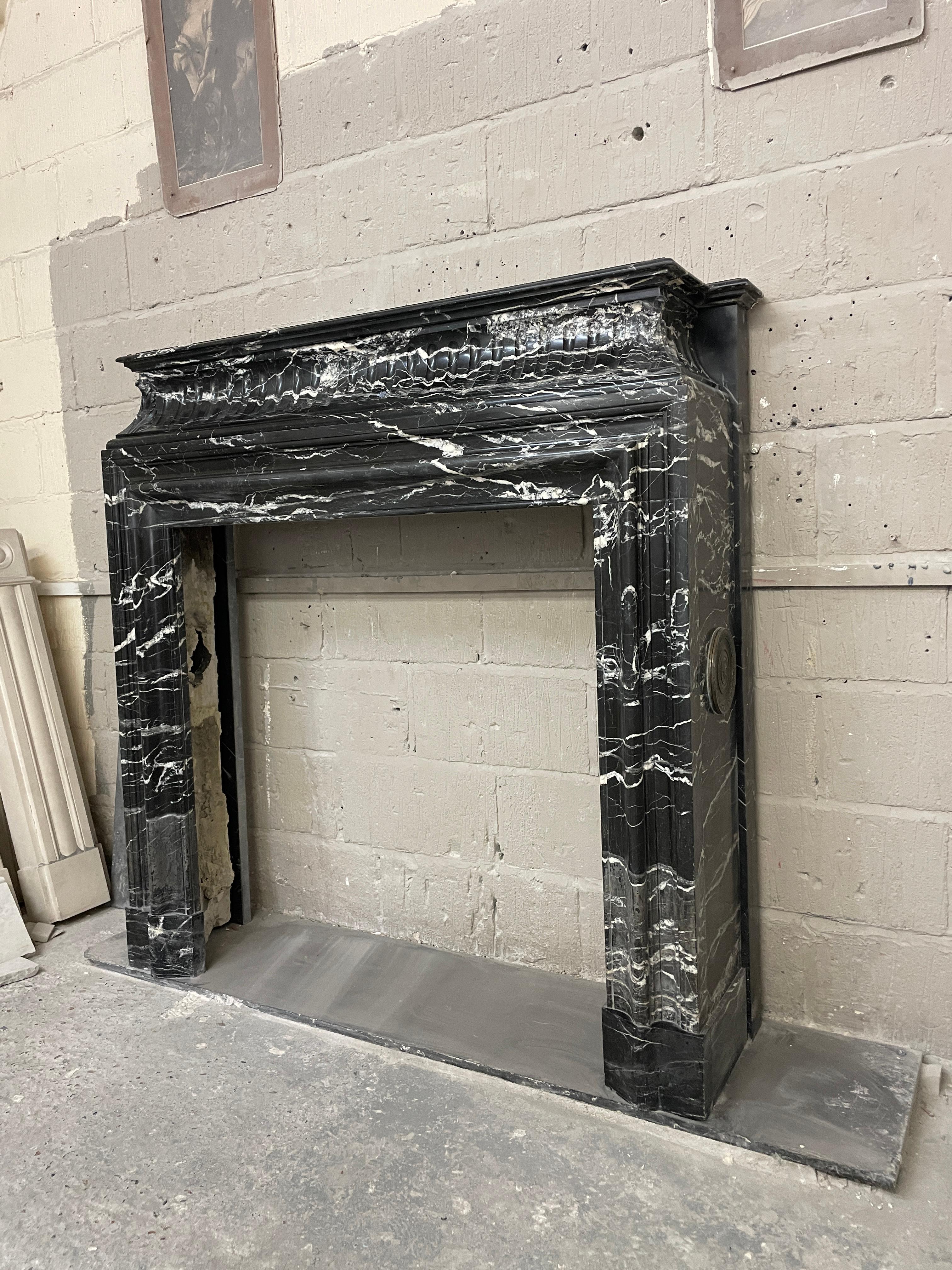 A substantial and very good quality French Louis XIV style fireplace in Italian antique Nero Marquina marble, variegated with large splashes of white. This 'Bolection de Versailles
