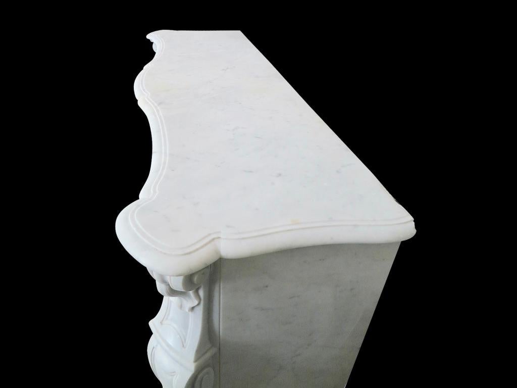 A good sized Louis XV style 19th century fireplace in Italian Carrara marble. The fielded cantered jambs with stiff carved Acanthus to bottom surmounting in C scrolls and shells at tops.
The frieze with carved cartouche at the centre of a plain
