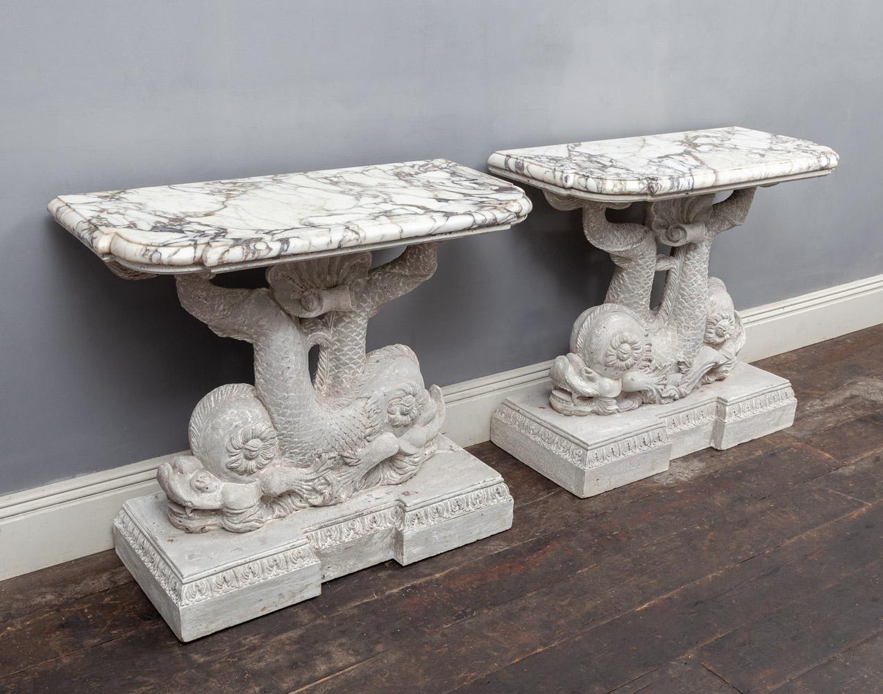 A magnificent antique pair of carved and painted wooden console tables, in the manner of William Kent. Two entwined stylized dolphins with centred scallop shells act as supports for the original Breccia Violetta marble tops. Their inapt faces,
