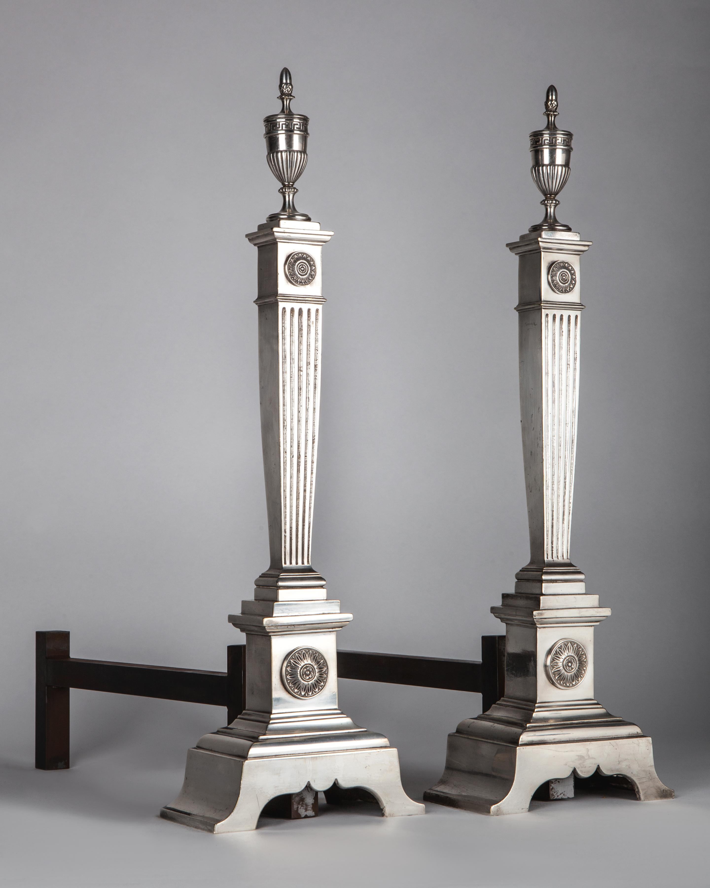 AFP0602
A pair of antique silver plate andirons with tapered square fluted column bodies on splayed bases surmounted by urn finials, circa 1910s.

Dimensions:
Overall 23-3/4