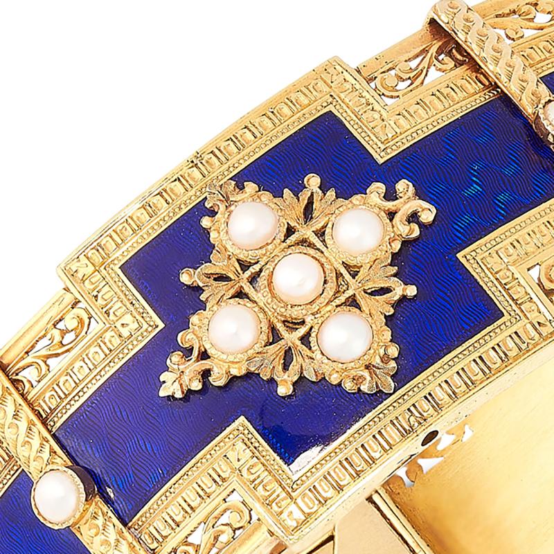 An antique pearl and enamel bangle, 19th century, the stylised body with pearl set motifs against translucent blue enamel over an engine turned guilloche background, within borders of egg and dart and pierced scrollwork decoration, French maker's