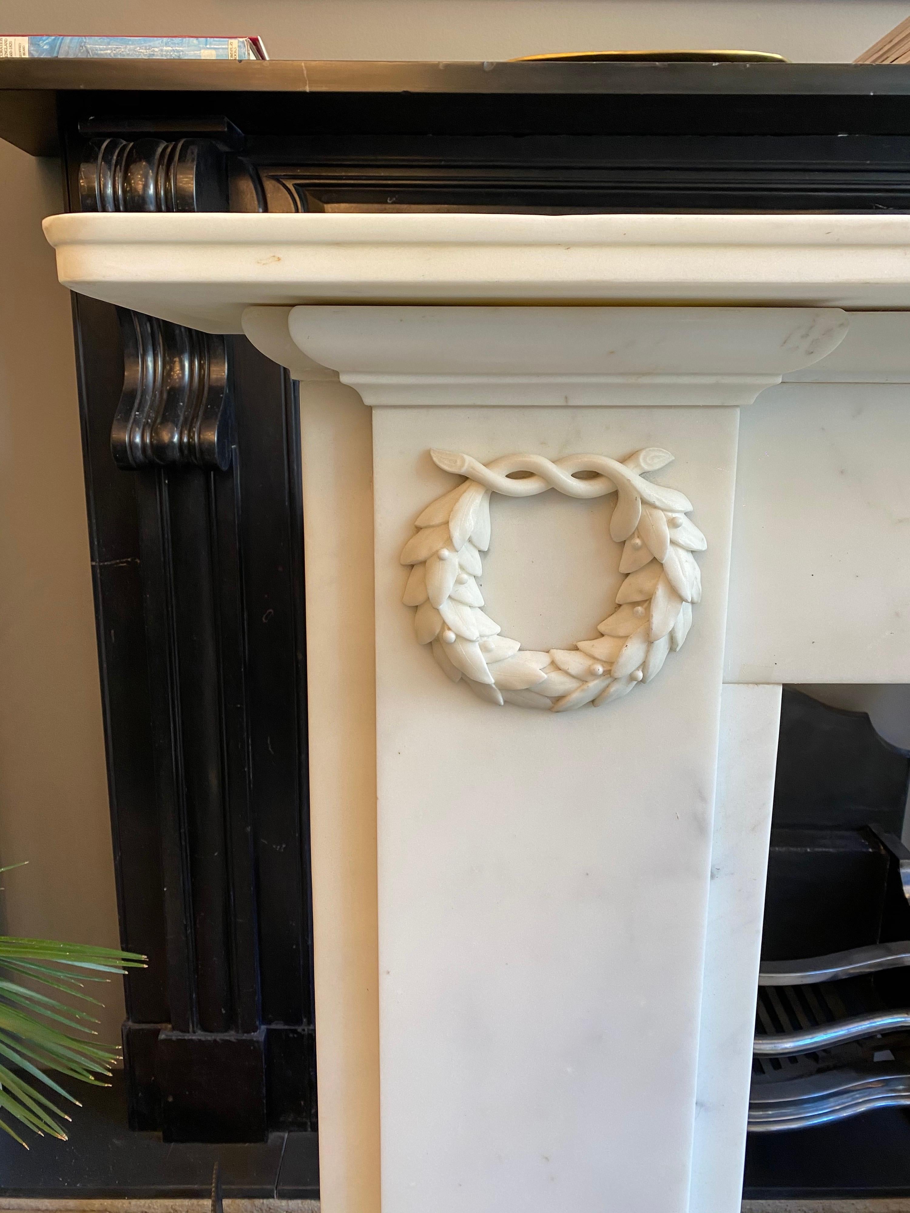 An elegantly simple English early 19th century statuary white marble fireplace, the plain pilaster jambs adorned with finely carved tied Laurels. A plain frieze, beneath a moulded shelf and standing on square foot blocks. A quality piece executed in