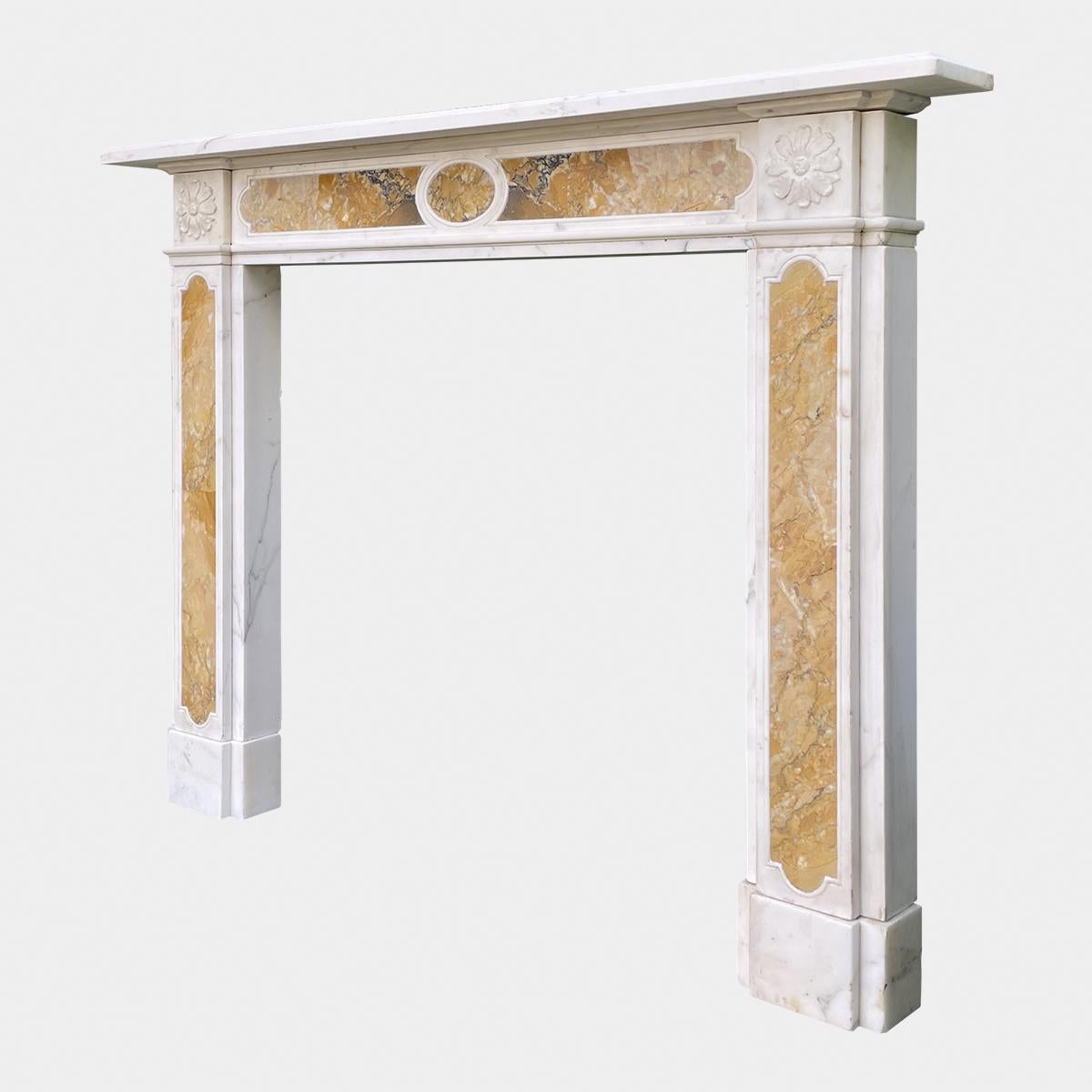 A Regency style fireplace from the mid 19th century executed in Italian Statuary white and Siena marbles. The jambs with inset Siena panels supported on foot blocks, terminating with carved rosette end blocks. The conforming frieze with carved