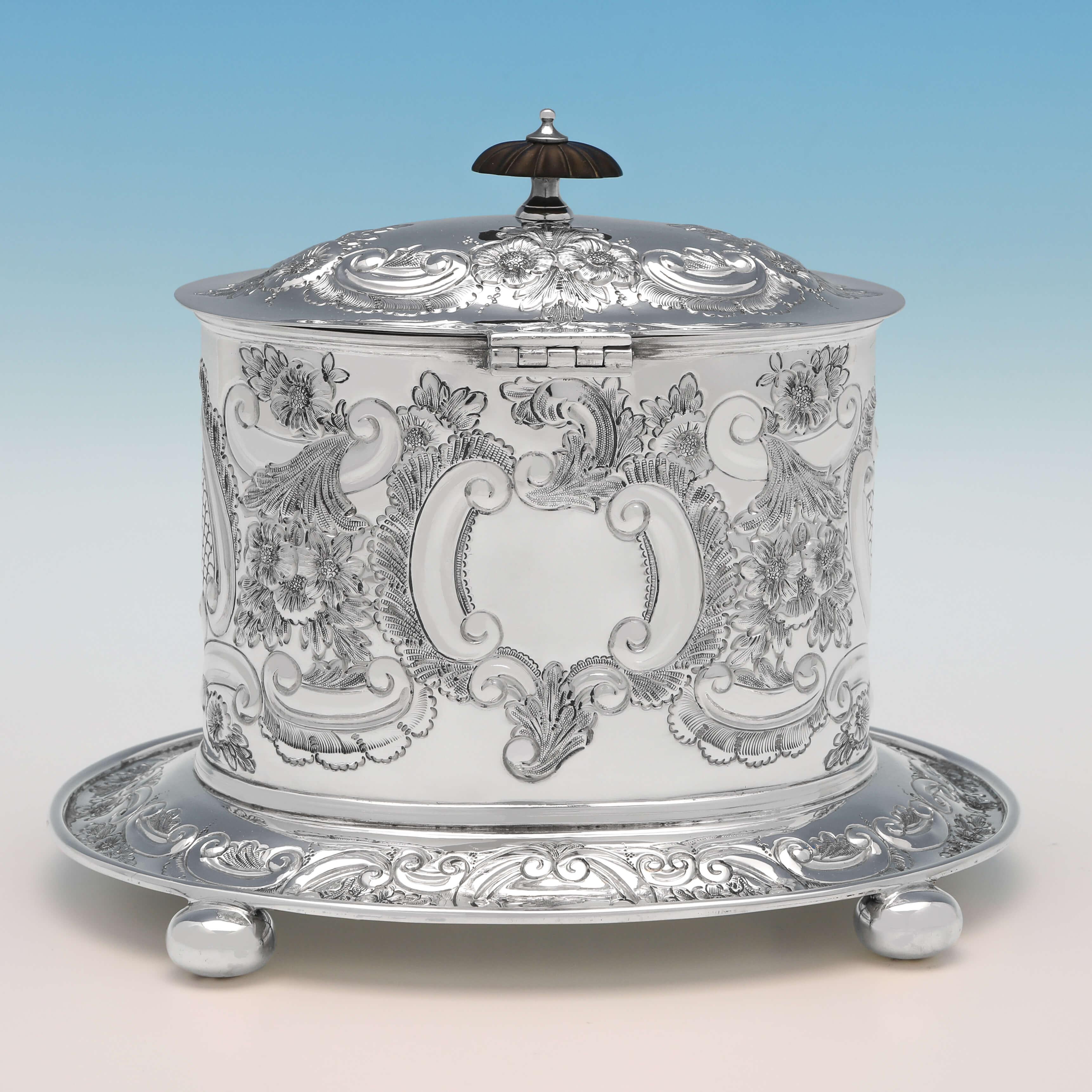 Hallmarked in Birmingham in 1901 by Thomas Latham & Ernest Morton, this very attractive, Victorian, antique sterling silver biscuit box, is oval in shape, standing on four ball feet, and featuring wonderful chased decoration throughout. The biscuit