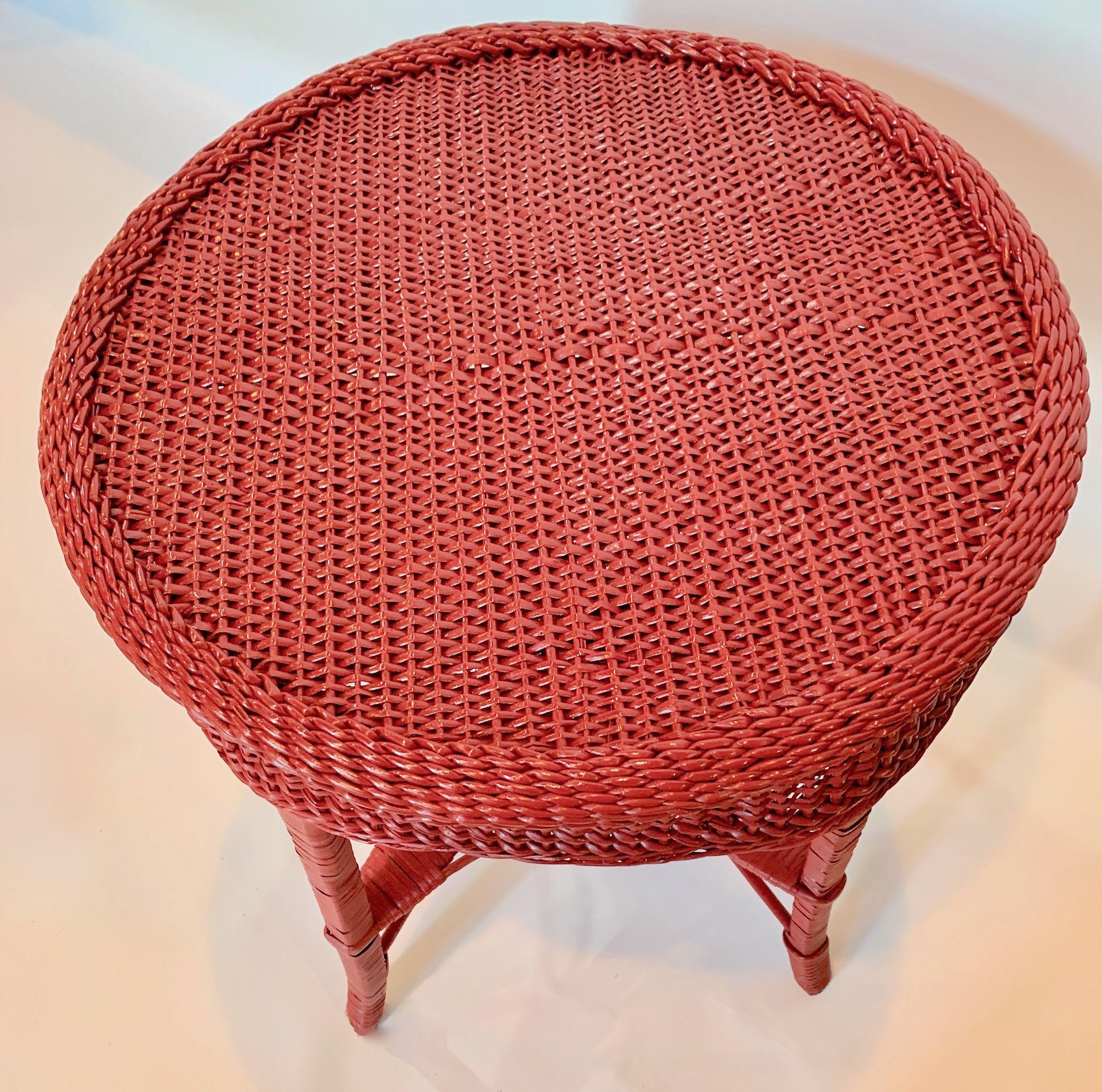 An early round wicker lamp table, American,C.1910 with red painted finish. The table is woven with flat woven wicker decorative top surrounded by an intricate woven braided trim above a substantial woven decorative skirt, The table is supported by