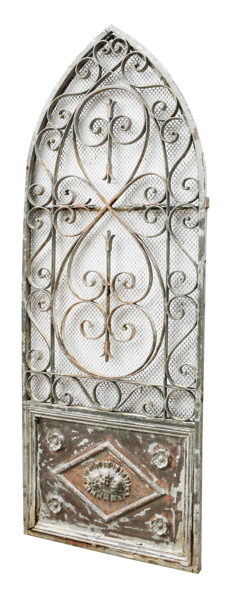 An antique arched wrought iron gate with scrolling pattern and a sheet steel panel with applied cast iron decoration. The wire mesh has been added later and can be removed if required.