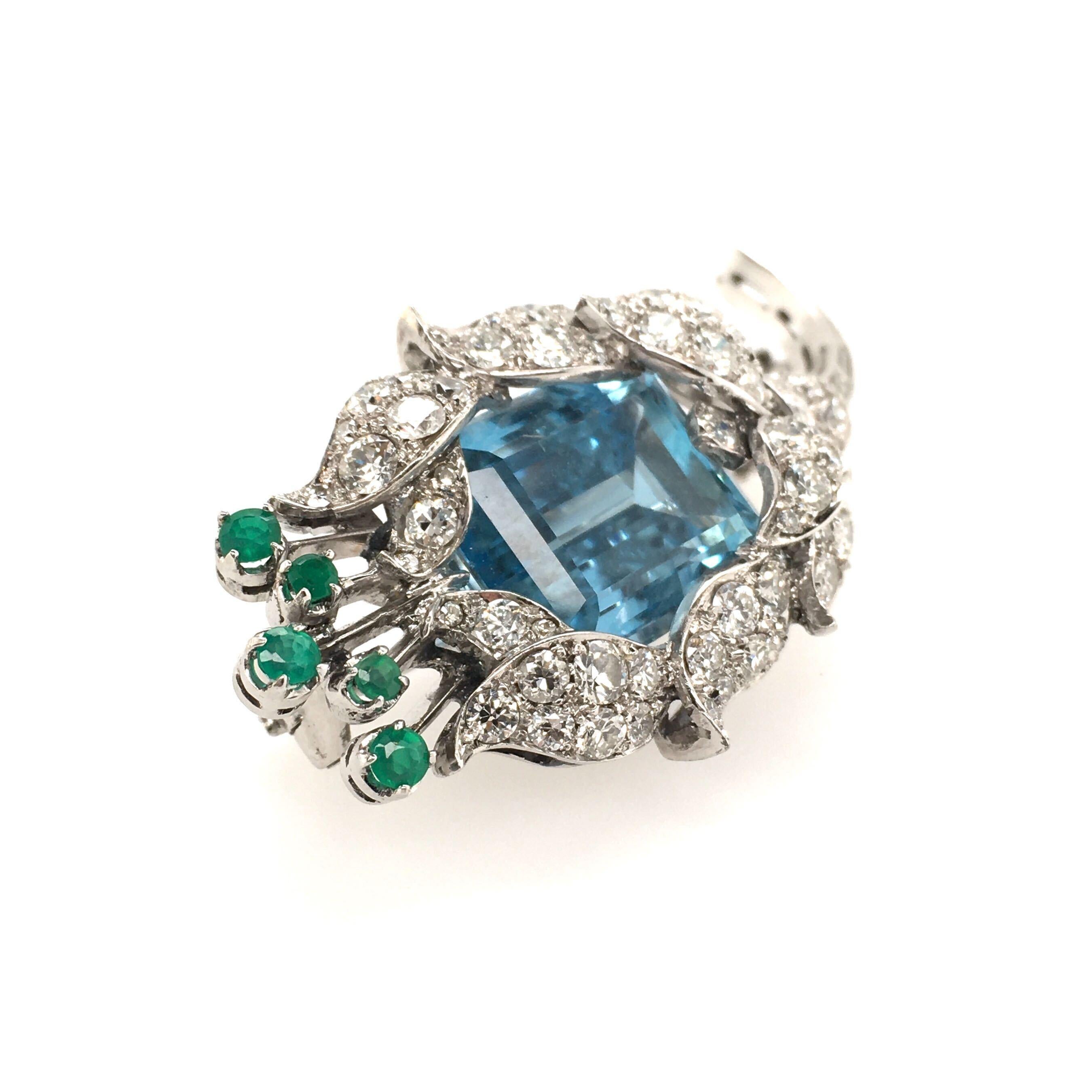 An 18 karat white gold, aquamarine, diamond and emerald brooch. Designed as a pave set diamond flower, centering an emerald cut aquamarine, measuring approximately 15.0 x 12.0 x 9.0mm, and weighing approximately 10.00 carats, enhanced by a baguette