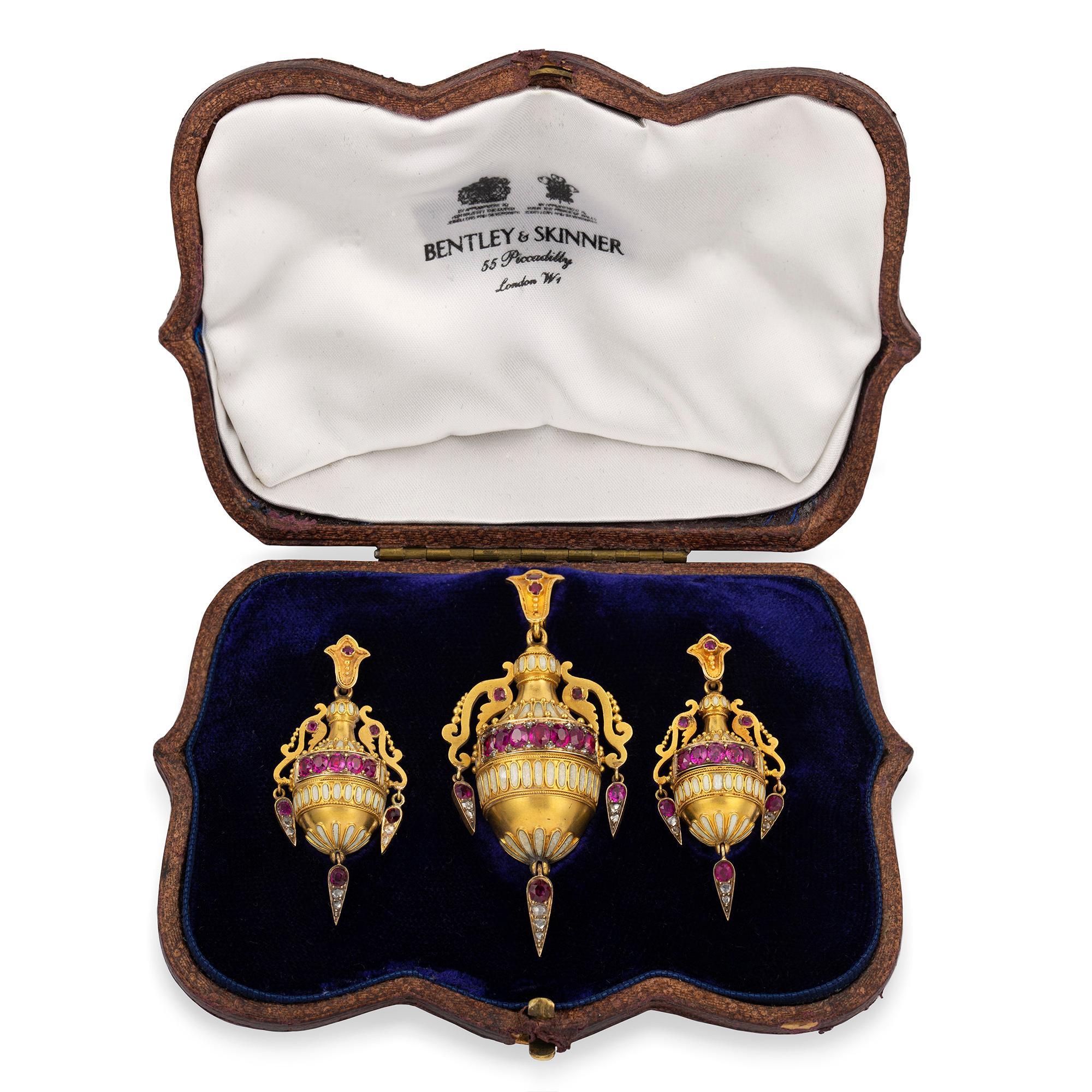 An arcaheological revival demi-parure, attributed to Guliano, consisting of a pair of earrings and  pendant in the form of amphorae, with fine wire-work and white enamel decorations, encrusted with faceted rubies estimated to weigh 3¾ carats in