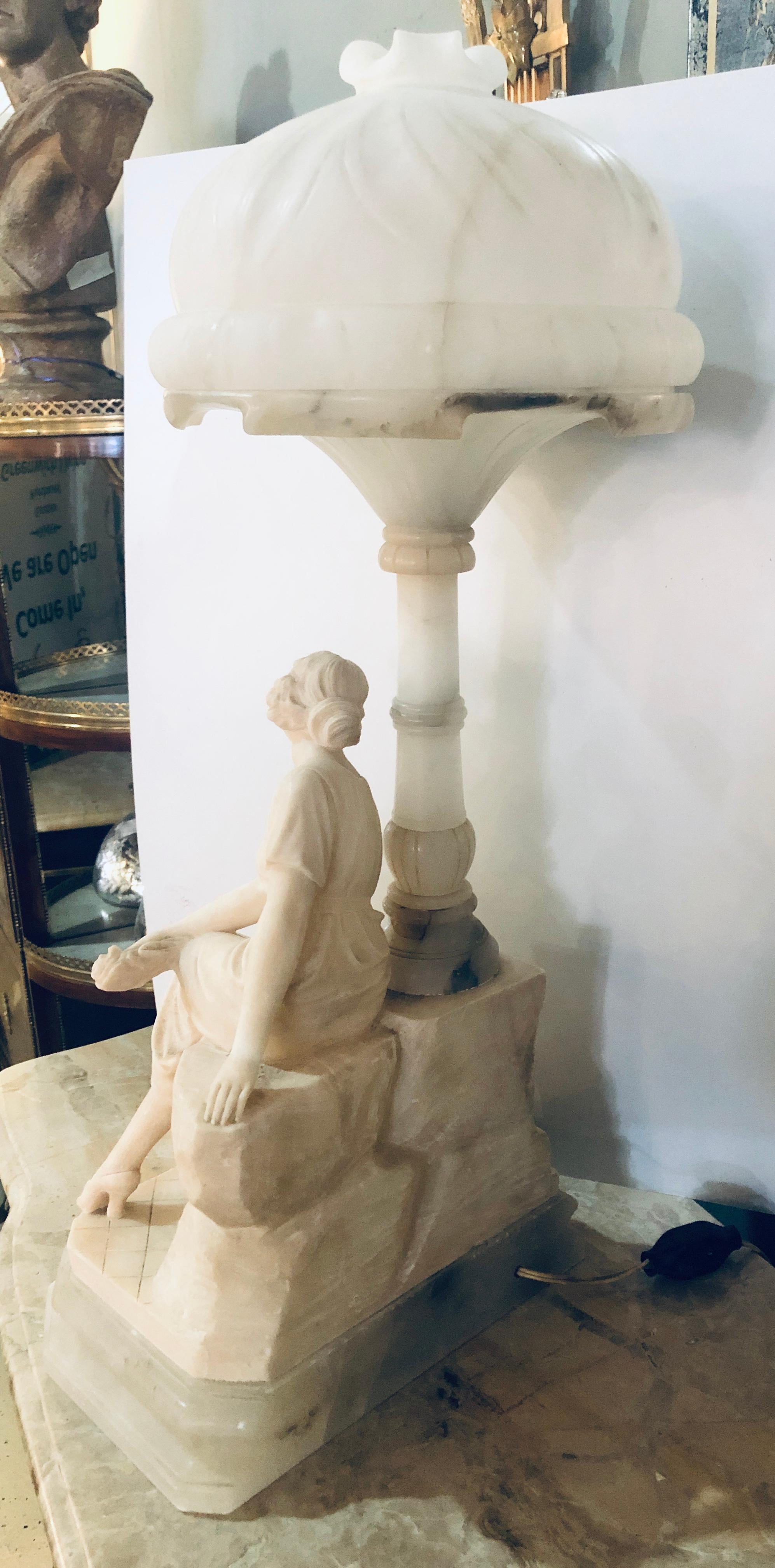Lámpara de sobremesa Art Decó con cúpula de alabastro. Bonita escultura de una mujer sentada sobre una farola. Después de una noche de baile, esta chica cancán tenía que descansar los pies de camino a casa. El interior o el globo que lleva una
