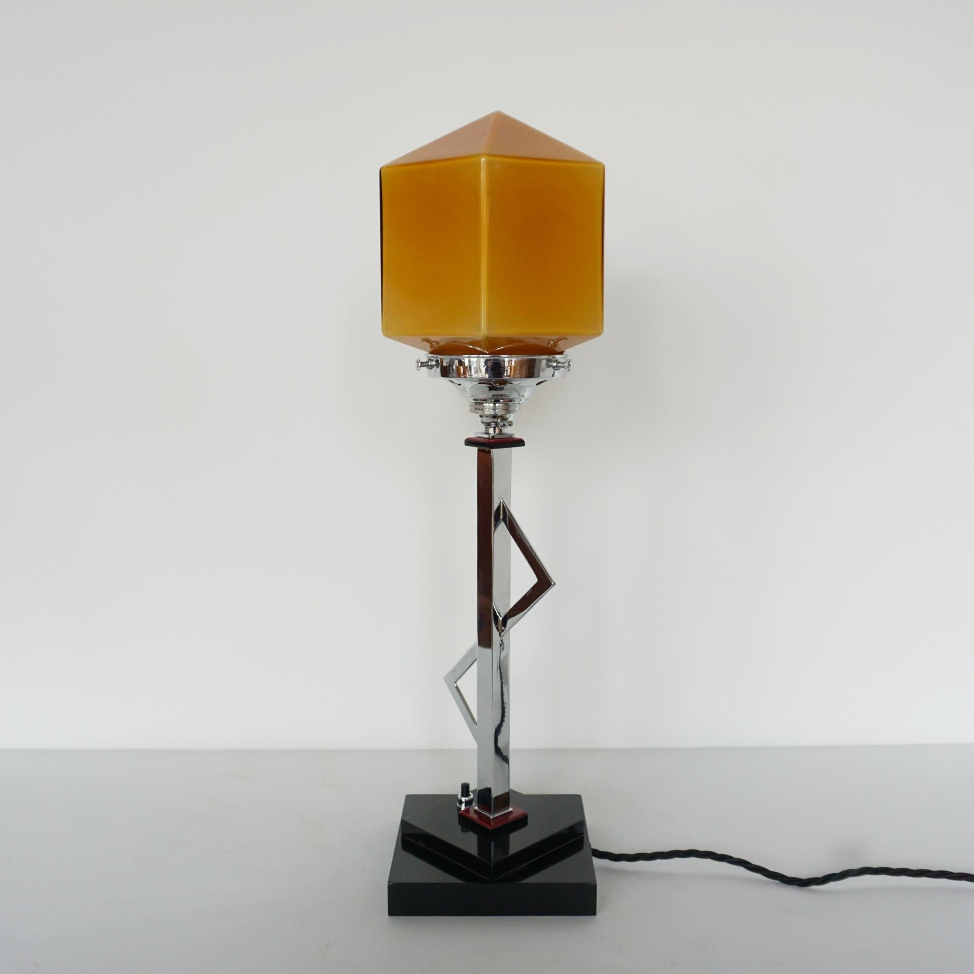 An Art Deco table lamp. Amber hexagonal glass globe set over a  stepped black bakelite base with an asymmetrical chromed stem.

Dimensions: H 50cm W 13cm

Origin: English

Item Number: J337

All of our lighting is fully refurbished, re-wired, and