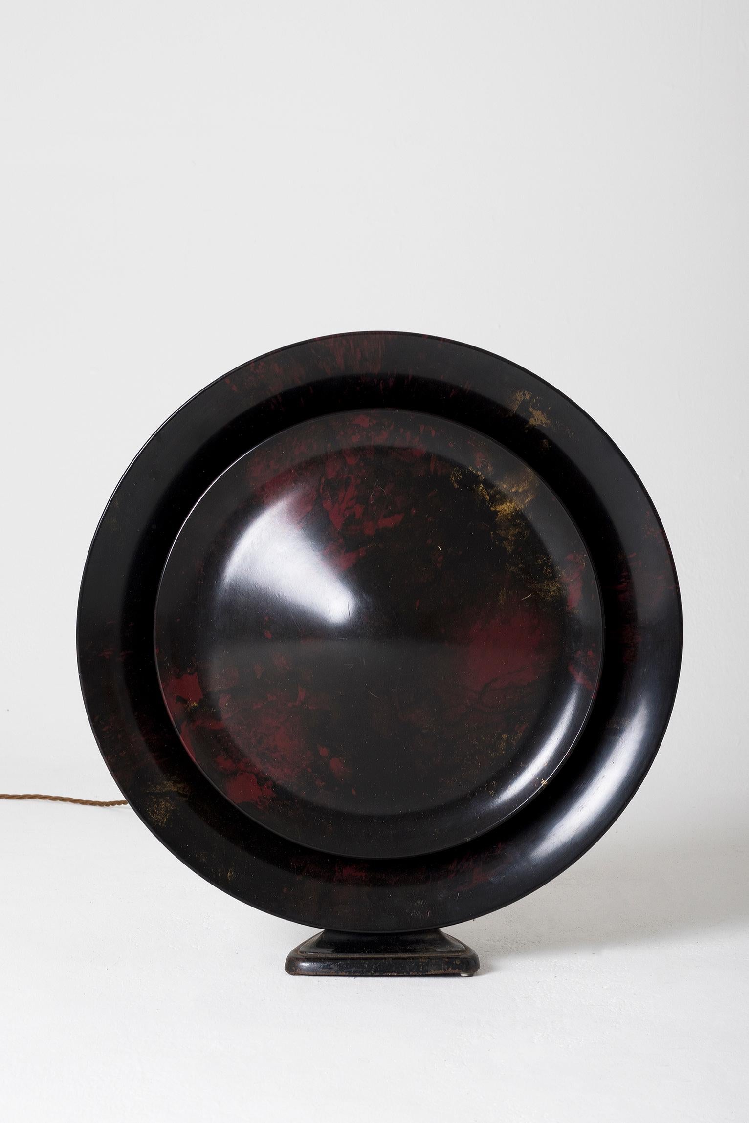 An Art Deco bakelite speaker converted into lamp, the internal lighting creating a solar eclipse like effect. 
The bakelite with inclusions of reds and gold, reminding Japanese lacquer Jingasas. 
France, circa 1930.