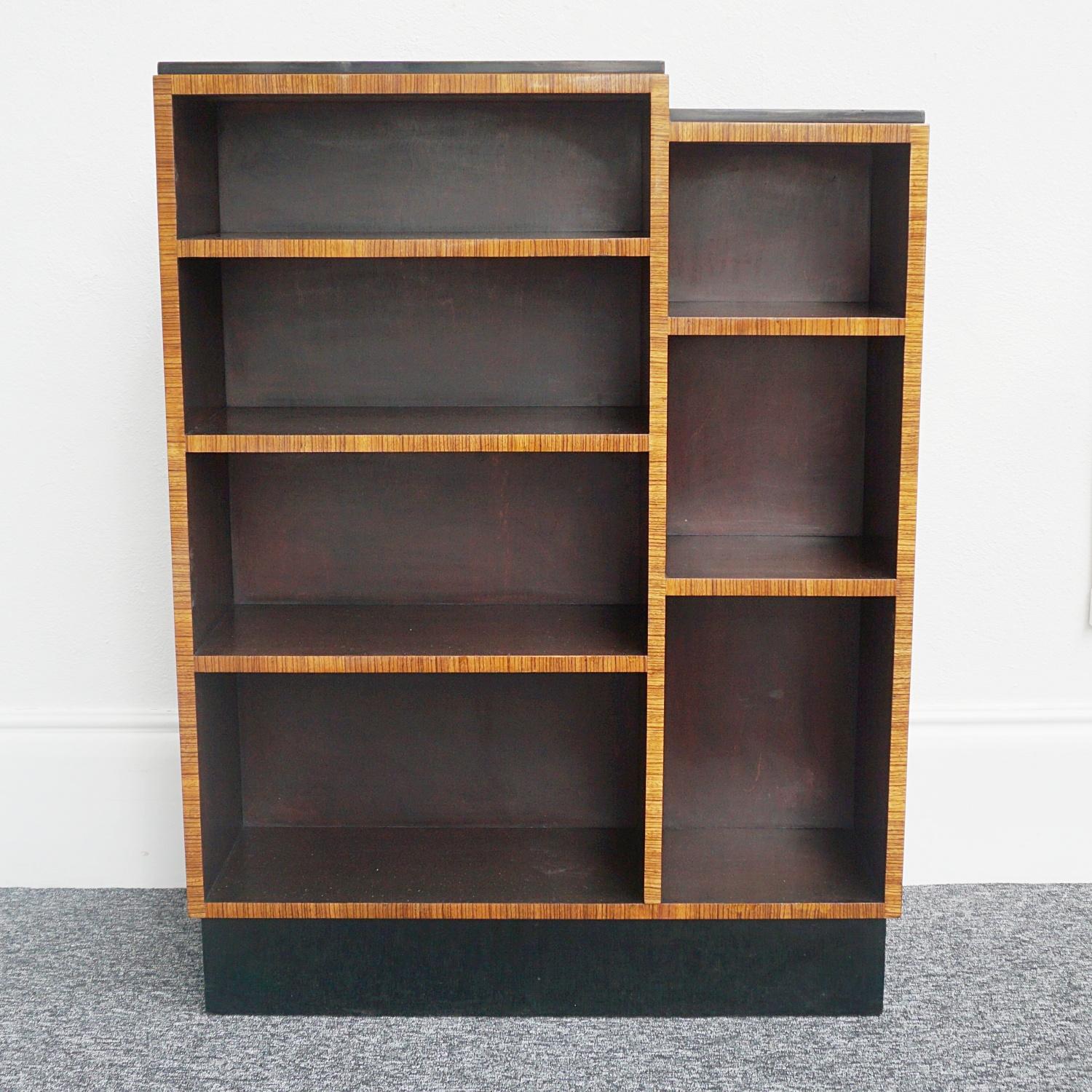 An Art Deco skyscraper bookcase. Birdseye maple veneer to top and sides with figured walnut front banding. Four graduating shelves to the left with three graduating high shelves adjacent. Ebonised banding to top with an ebonised base.