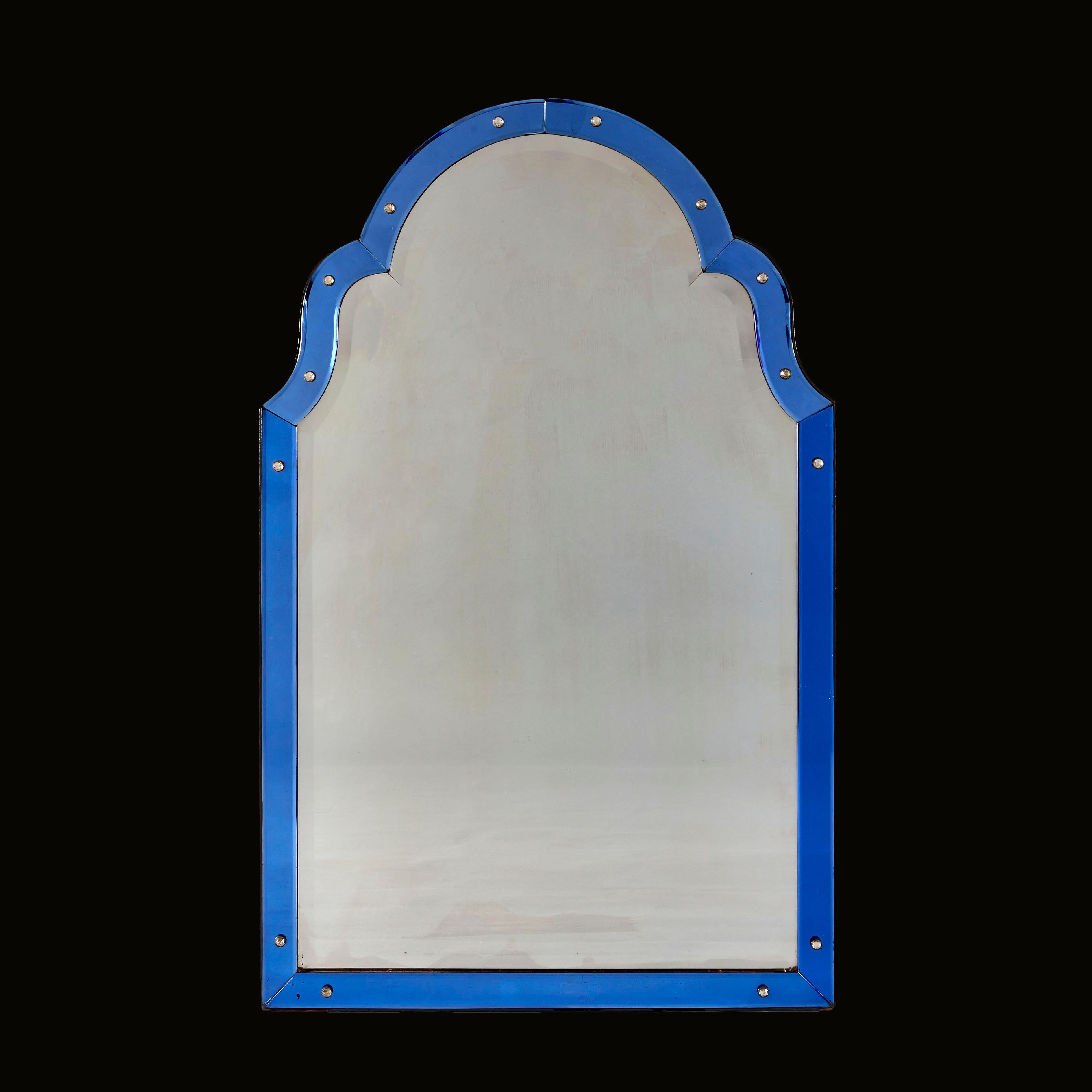 A striking Art Deco mirror with arched pediment, the central shaped and beveled plate framed by blue glass borders with beveled edges and clear glass paterae studs.