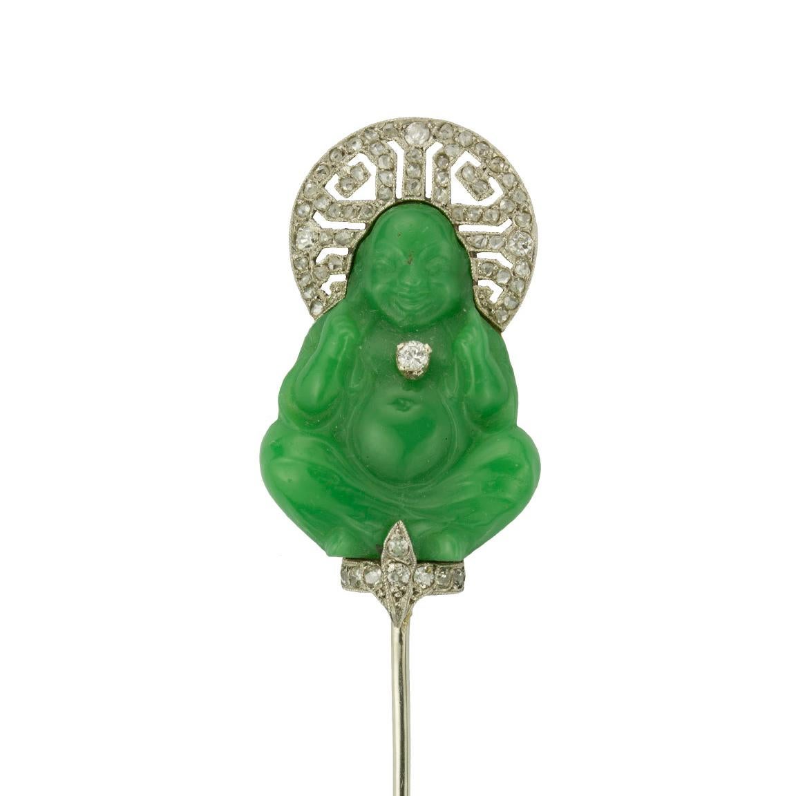 An Art Deco Buddha sureté pin, set with a green pâte de verre Buddha, resting upon a diamond fleur-de-lis pedestal, with a platinum hallo-shape crown and a single diamond pendant, all to a platinum and white gold mount, encrusted with rose-cut and
