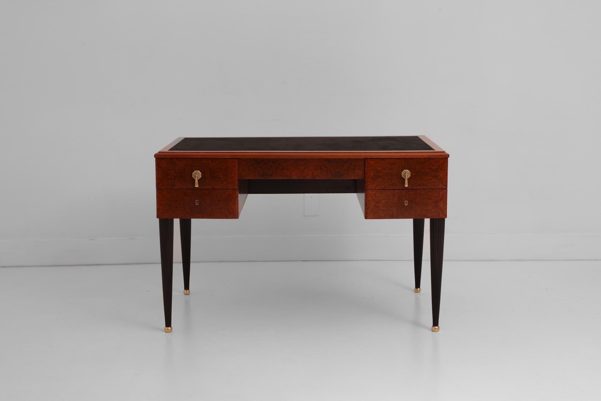 This fine Art Deco desk is a true gem. The desk is veneered in a warm burled wood. The fluted legs have been lacquered black and are finished with a round brass sabot. The stylish brass pulls are decorated in a classic Art Deco motif. The top of the