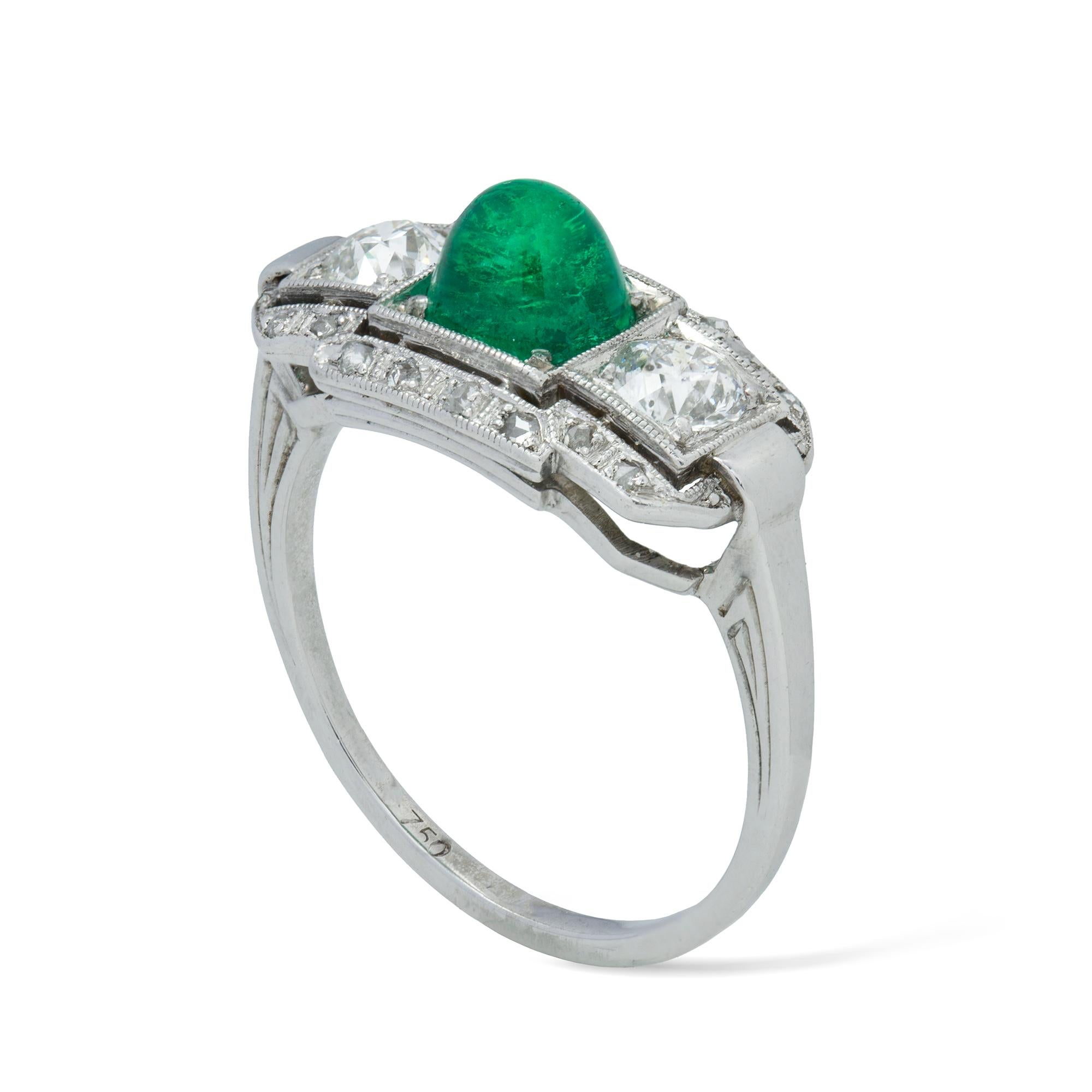 An Art Deco cabochon emerald and diamond ring, the central cabochon cut emerald estimated to weigh 1.1 carats accompanied by GCS Report stating that is of Colombian origin, flanked by two old brilliant-cut diamonds, surrounded by a row of small rose
