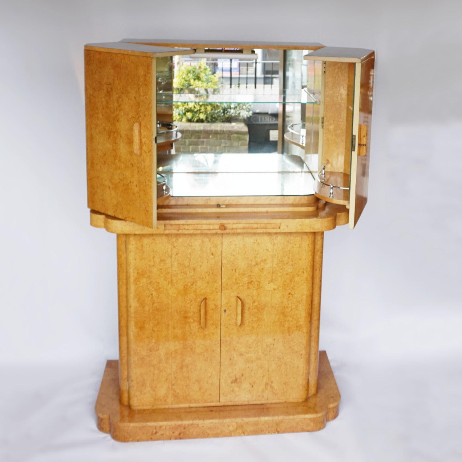 An Art Deco cocktail cabinet by Harry & Lou Epstein. Bleached burr walnut veneered on solid walnut and mahogany. Upper mirrored lit section with glass shelf. Mirrored pull out tray with original amber bakelite handle. Lower section opens to bottle