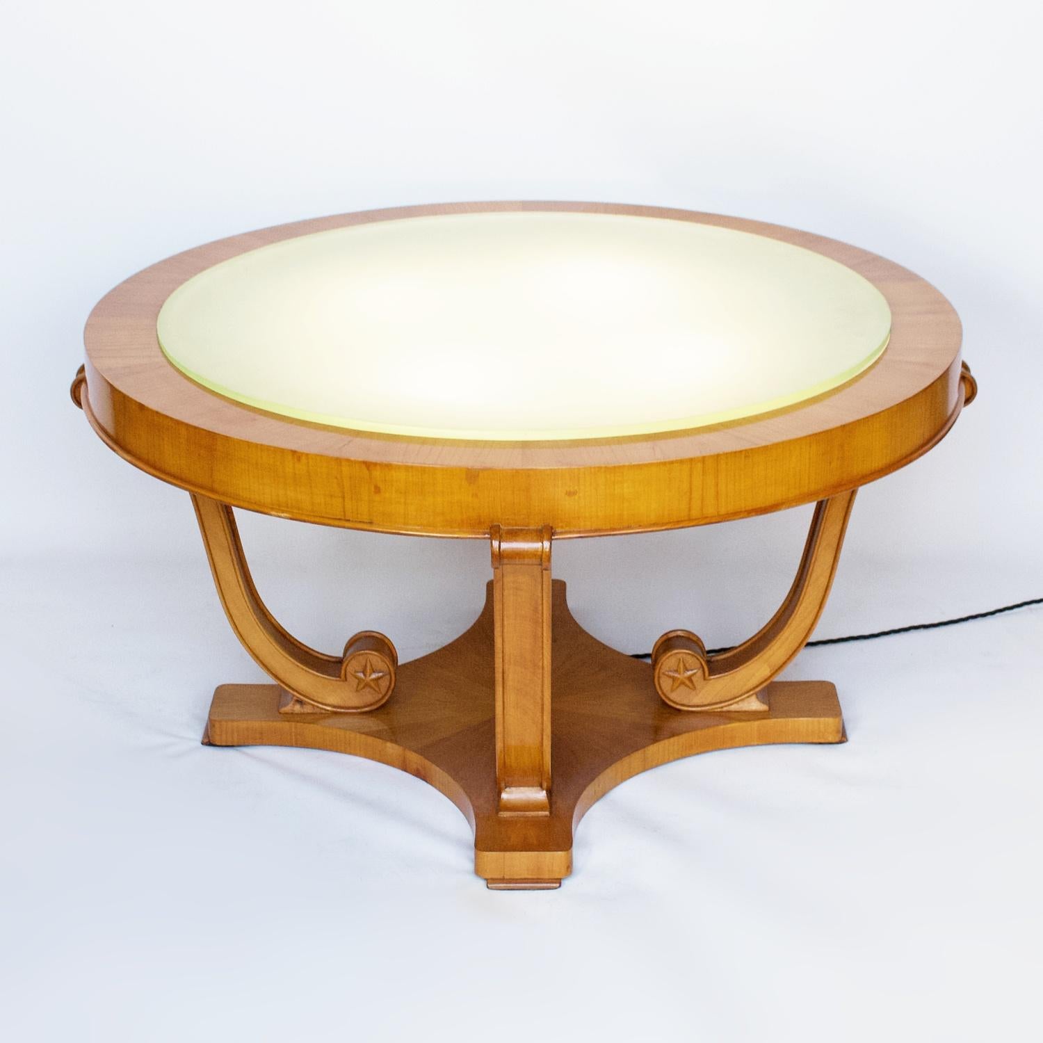 An illuminating Art Deco coffee table by De Coene. Four light points underneath a sandblasted green, blue glass table top. Satin Birch frame is connected to the base by four curved legs with carved star details.
