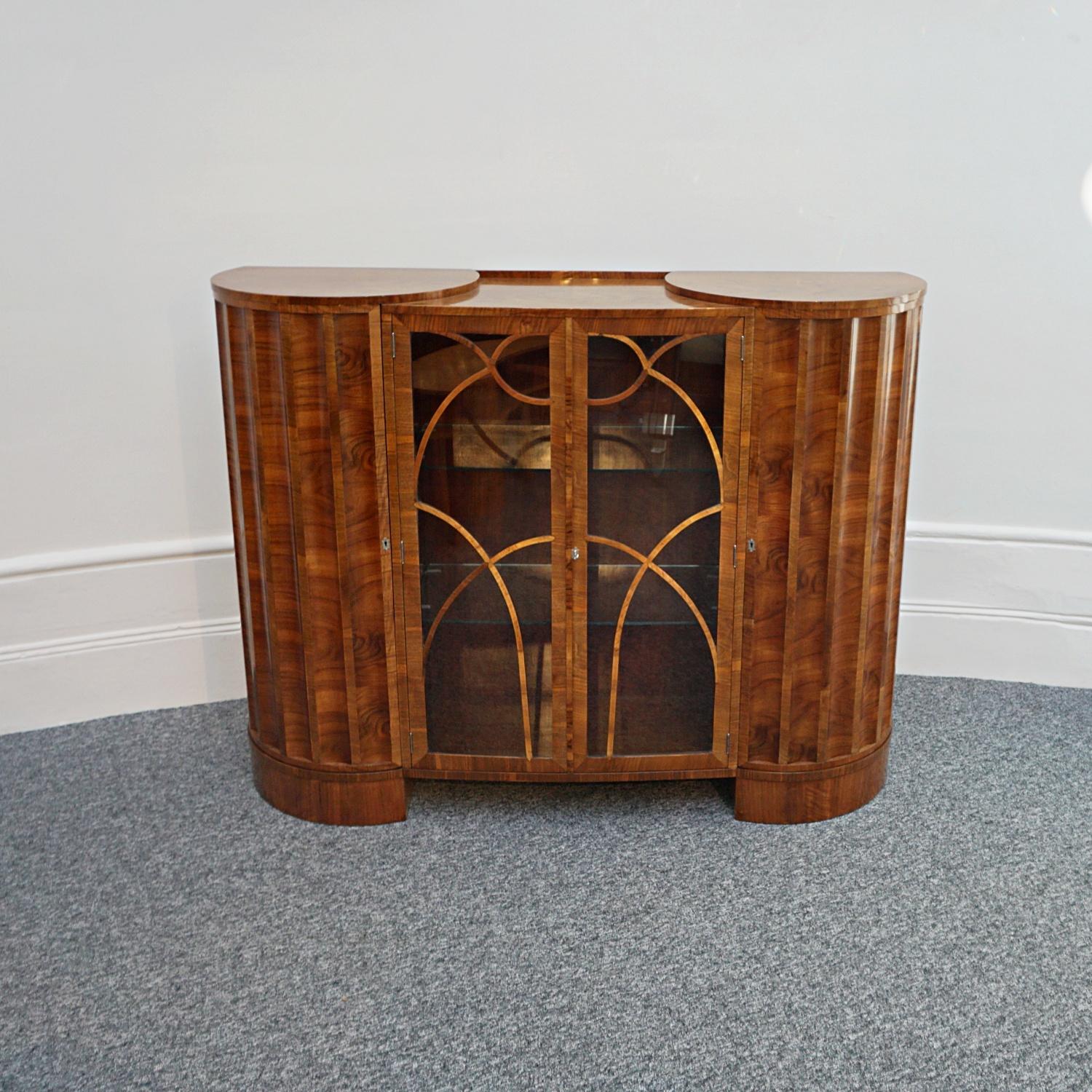 An Art Deco cabinet. Curved and fluted doors to side with a central glass fronted section withAn Art Deco Cabinet. Curved and fluted doors to side with a central glass fronted section with figured walnut shaped banding. The central section with