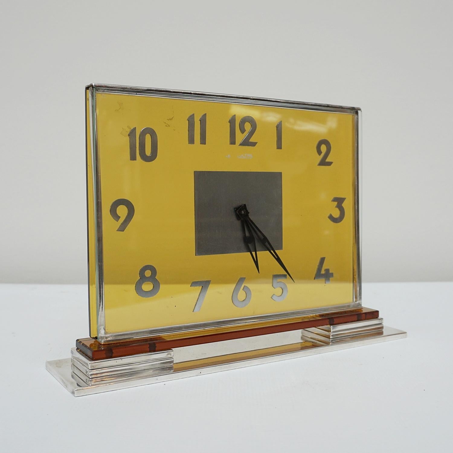 An Art Deco Desk Clock by Jaeger Le-Coultre. Yellow tinted glass face with arabic numerals, raised on a stepped chrome base with an amber glass surround. 

n 1903, Paris based watchmaker Edmond Jaeger set a challenge for Swiss manufacturers to