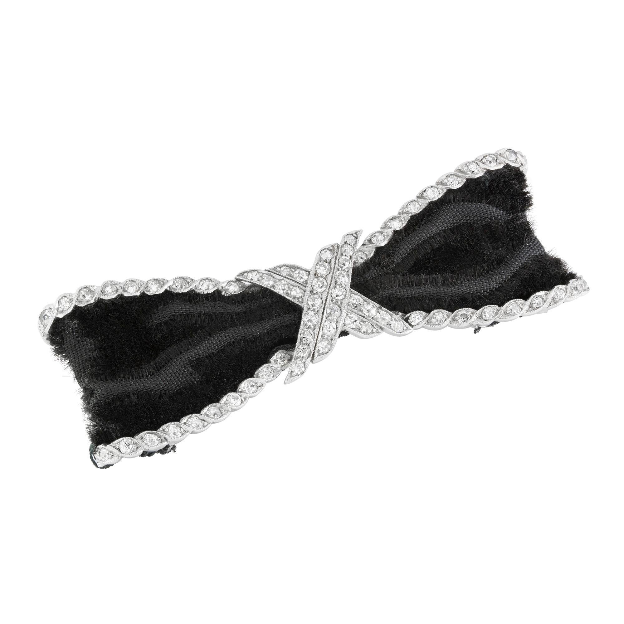 An Edwardian diamond bow brooch, the open ribbon tied bow with old-cut diamond set cross-over centre and diamond set barley twist border with black velvet ribbon to each loop, measuring approximately 5.3cm, circa 1910, gross weight 9.2 grams.

This