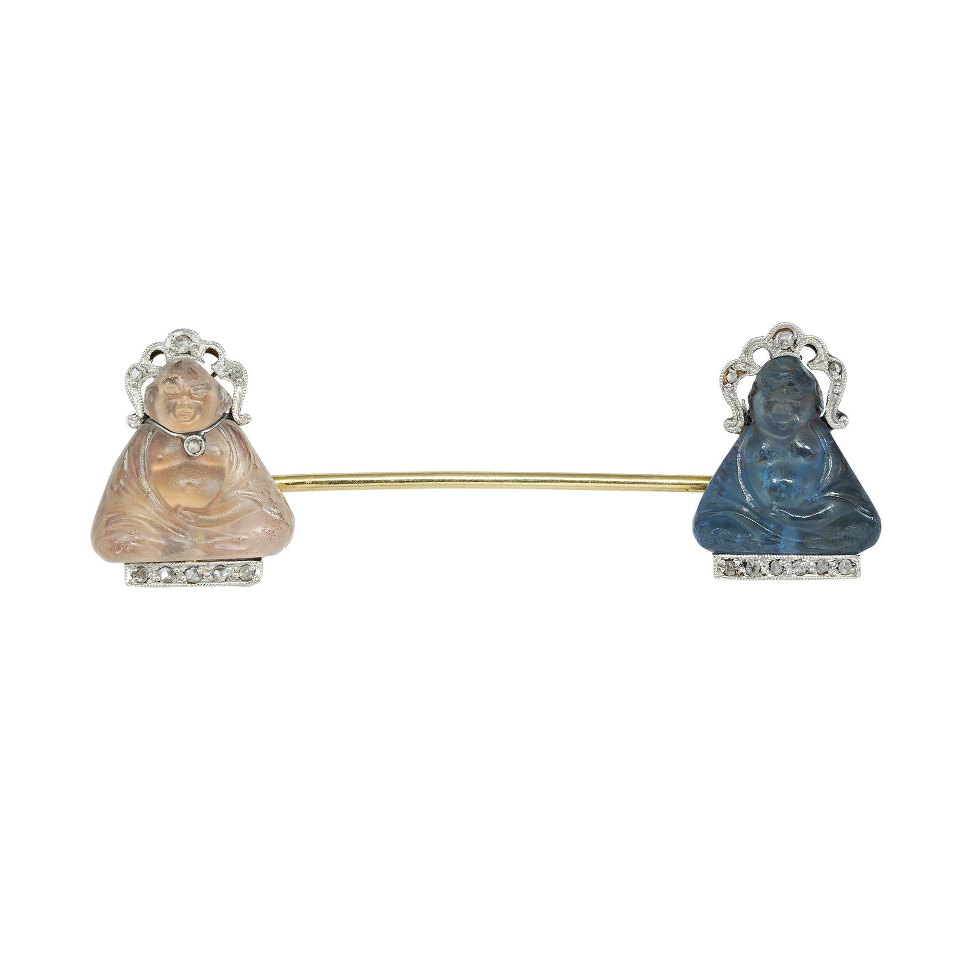 An Art Deco double Buddha jabot pin, with a blue and a white pâte de verre Buddhas, each embellished with rose-cut diamond-set halo and base, the white one bearing also a pendant, all set in platinum and gold, possibly French circa 1920, measuring