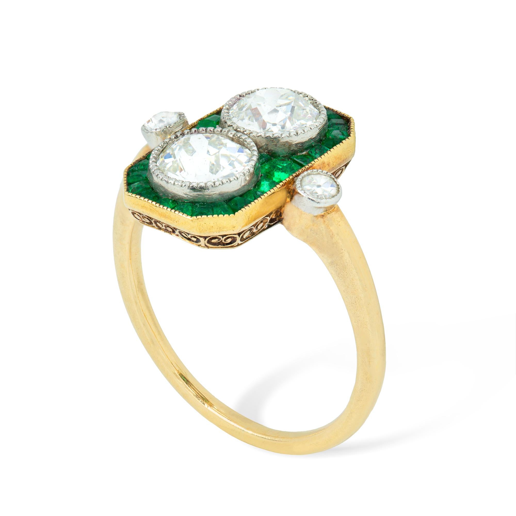 An early Art-Deco emerald and diamond plaque ring, the elongated octagonal plaque set with two old brilliant-cut diamonds in a fine millegrain setting, surrounded by thirty calibre-cut emeralds, to a gold millegrain setting, to a yellow gold