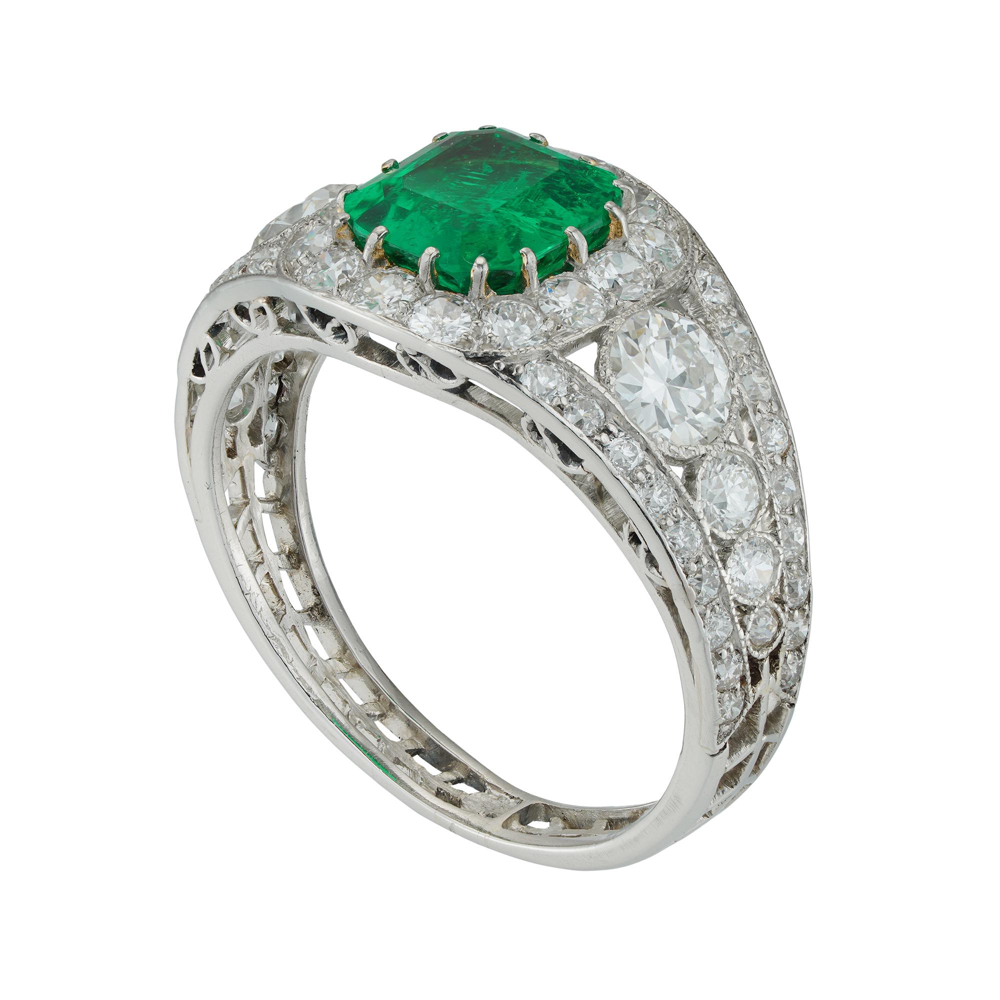 An Art-Deco emerald and diamond ring, the octagonal-cut emerald weighing 1.50 carats, accompanied by GCS report stating to be of Colombian origin, surrounded by fourteen old brilliant-cut diamonds, the openwork-design shoulders, each set with four