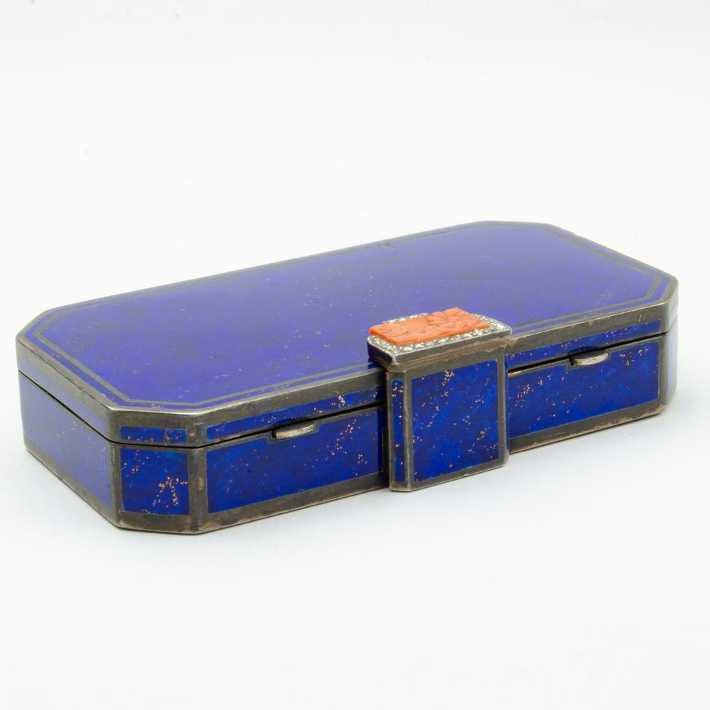The rectangular-shaped blue enamel vanity case with silver-coloured enamel borders and carved Coral and rose-cut diamond clasp opening to reveal a mirror, two powder compartments and a lipstick holder, circa 1920