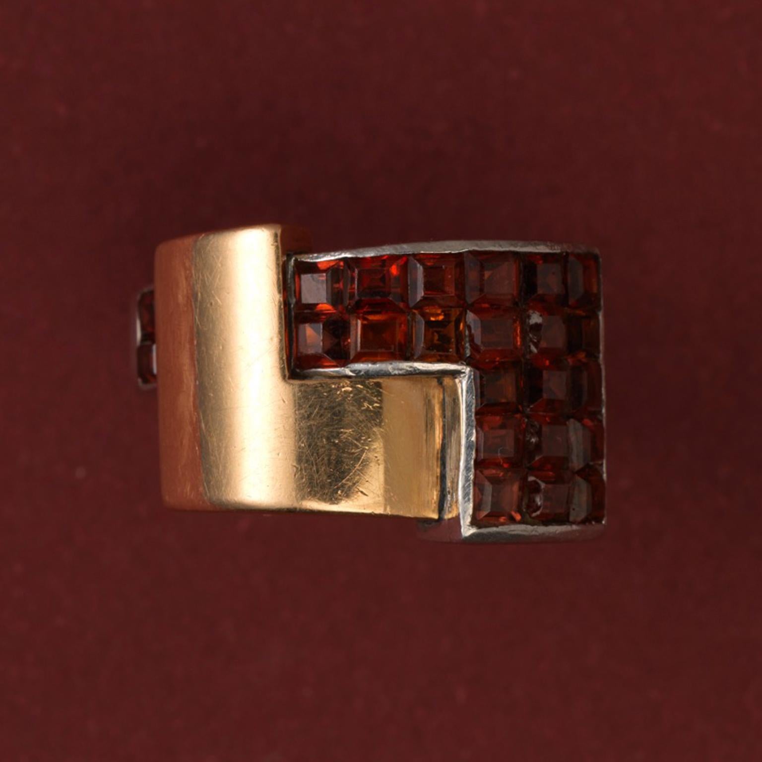 A rare Art Deco 18 carat gold and platinum ring in a geometrical construct of two juxtaposed angled elements, one in 18 carat gold and the other in platinum with 21 square-cut invisibly set hessonite garnets (app. 3.6 carats); master mark and