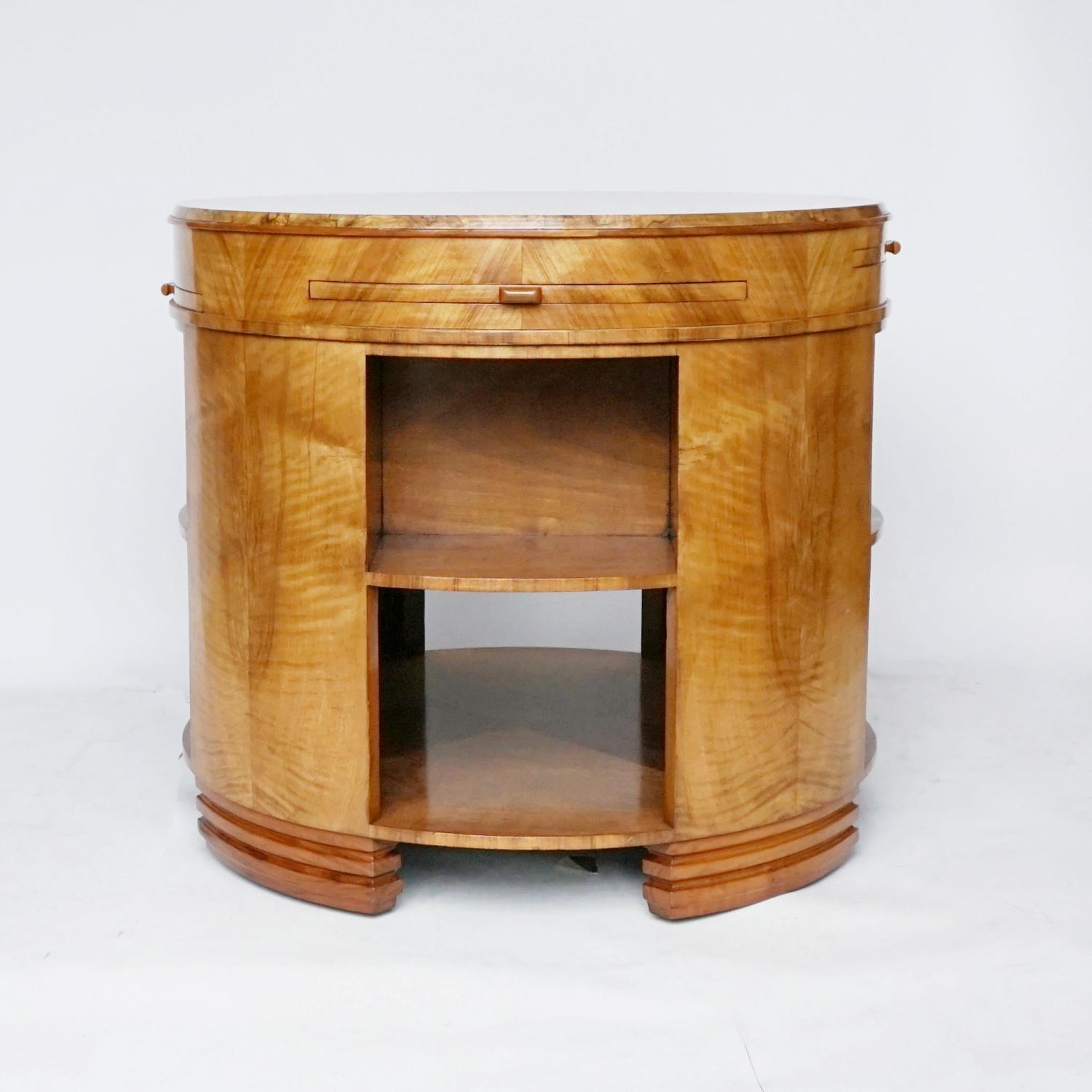 An Art Deco library table retailed by Heal's of London. Circular table with upper book shelves and lower open storage shelf. Four graduating pull out trays veneered in Birdseye Maple. Fantastic burr walnut veneered top with Figured walnut