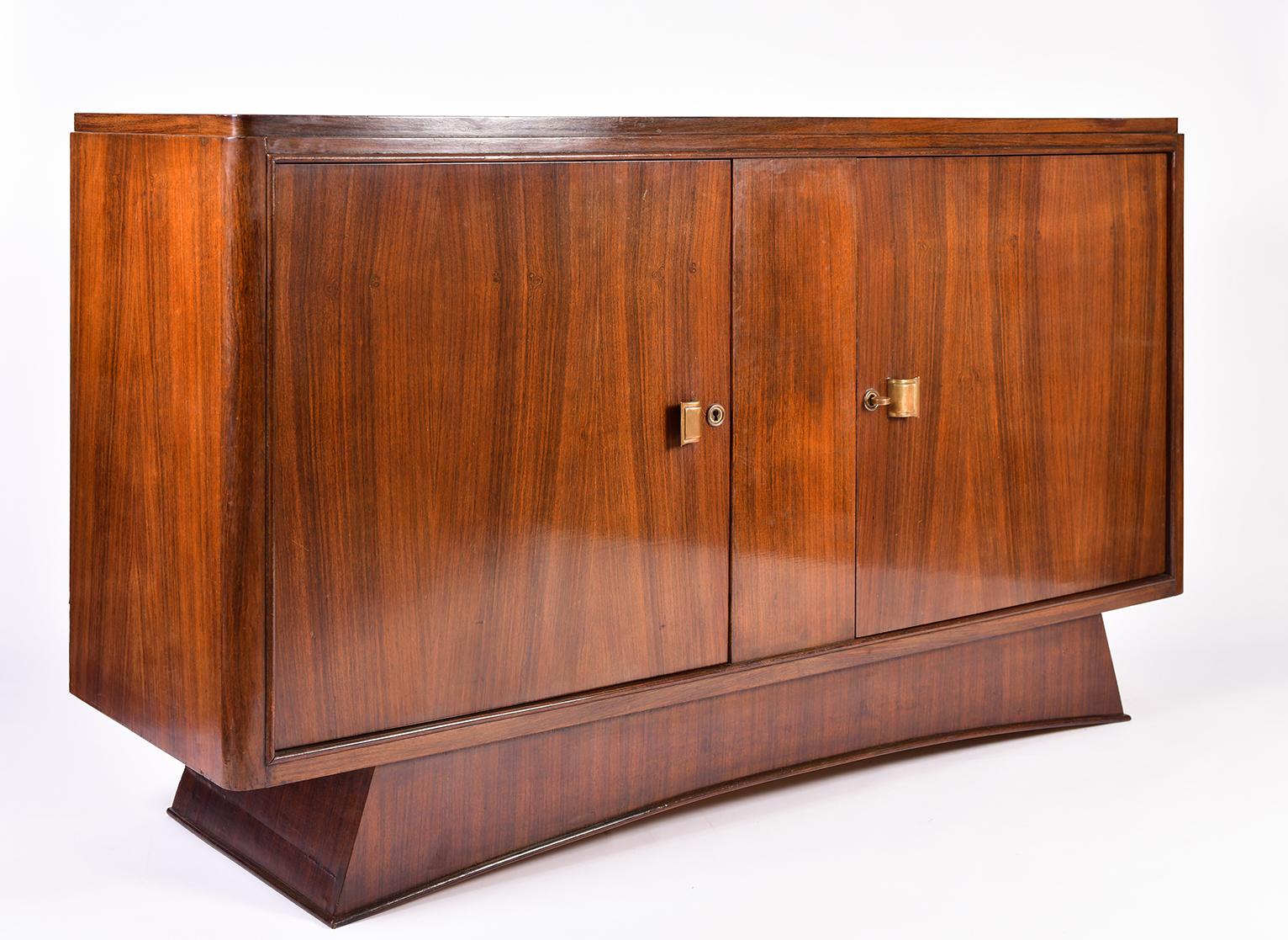 An Art Deco mahogany sideboard, on a bowed base, the two doors with shaped brass handles and the original key, revealing an oak fitted interiors, with an adjustable shelf and a drawer, adorned with geometric marquetry.
France, circa 1930.