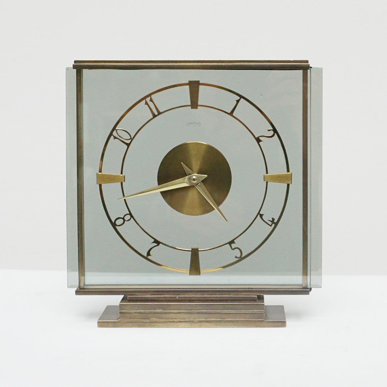 An Art Deco clock by Smiths. Glass panel with brass dial and numerals. Set over a stepped base.
