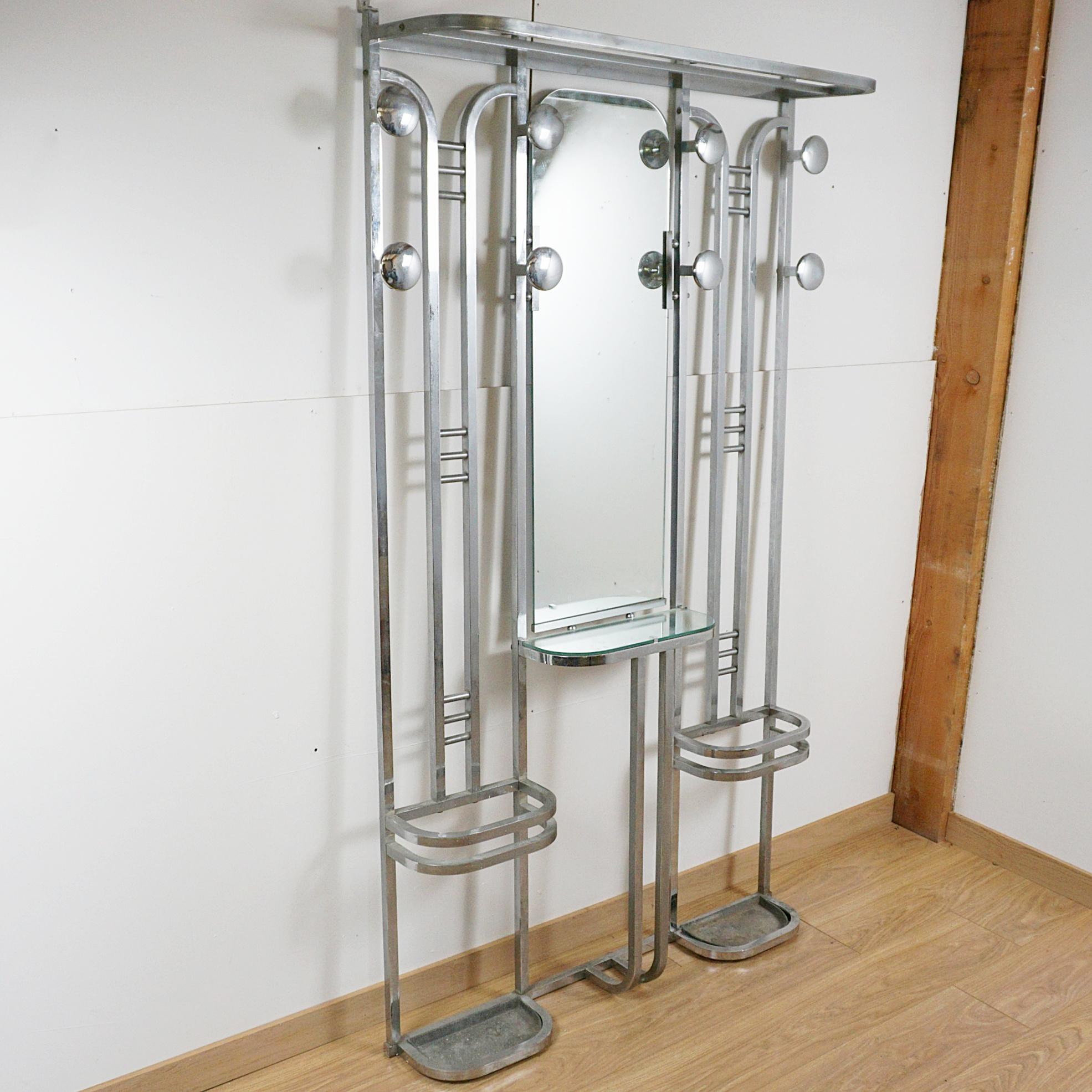 Un portaoggetti modernista in stile Art Déco. Struttura cromata lucida con consolle centrale a specchio, appendiabiti superiori, appendiabiti e portaombrelli ai lati. 
