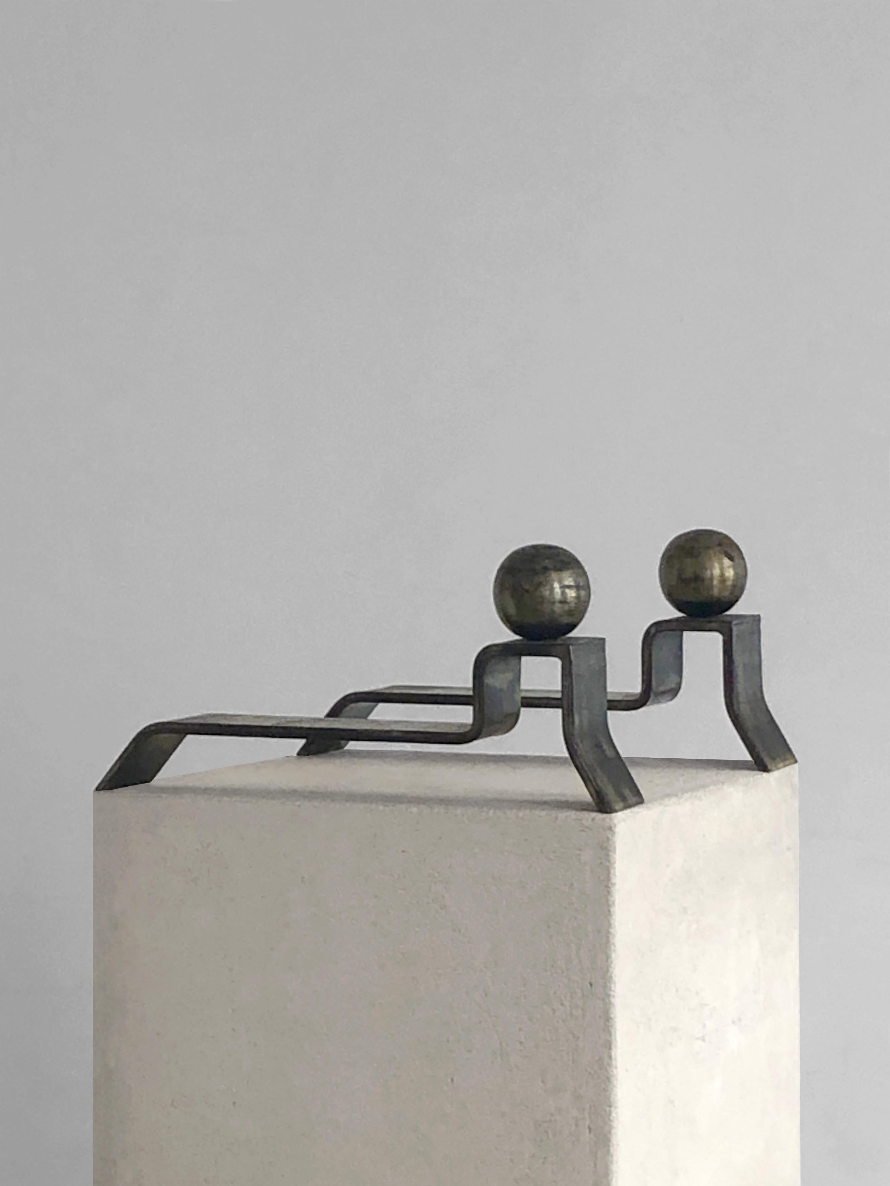 An impressive and luxurious pair of andirons, in the spirit of the best french modernist designers, to be attributed, France 1950. 
Each piece consists in one single thick and sensual slide of wrough iron topped by a massive bronze sphere, at the