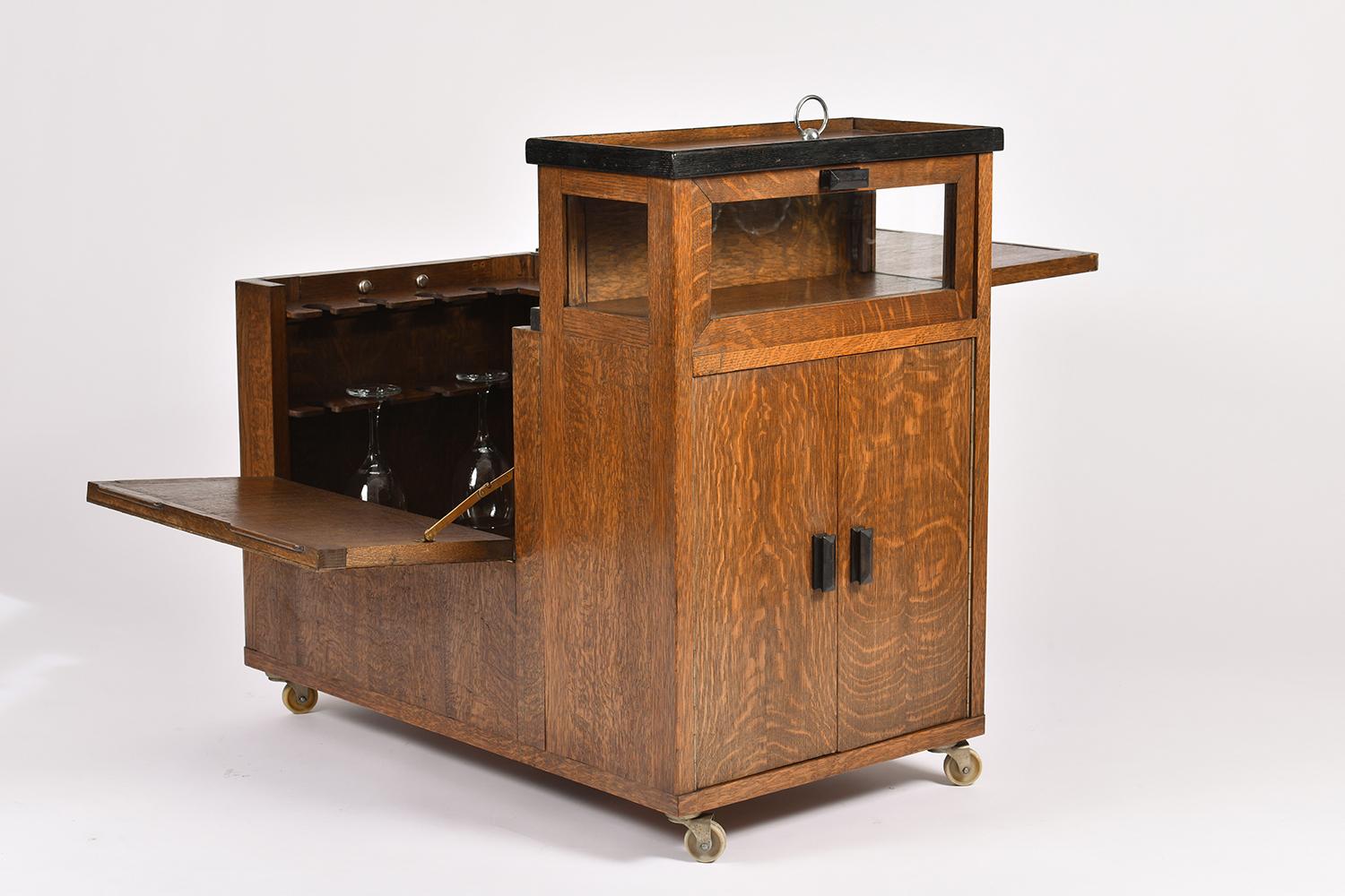 An Art Deco oak drinks trolley, the main compartment opening up to reveal 24 glasses holders and a removable ice cubes bucket, the other side with a glazed compartment above a two-door bottles.
France, circa 1930.