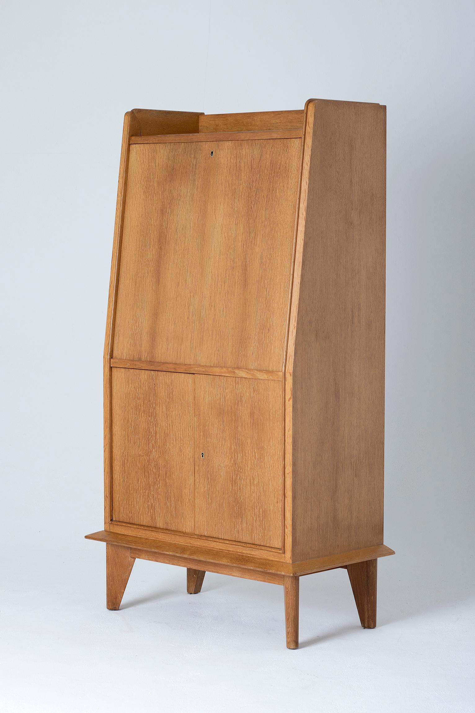 An Art Deco oak secrétaire cabinet, the abattant revealing a fully fitted oak secrétaire with pigeon holes, shelves and drawers with brass knobs, and a cream leather desk top.
France, circa 1940.