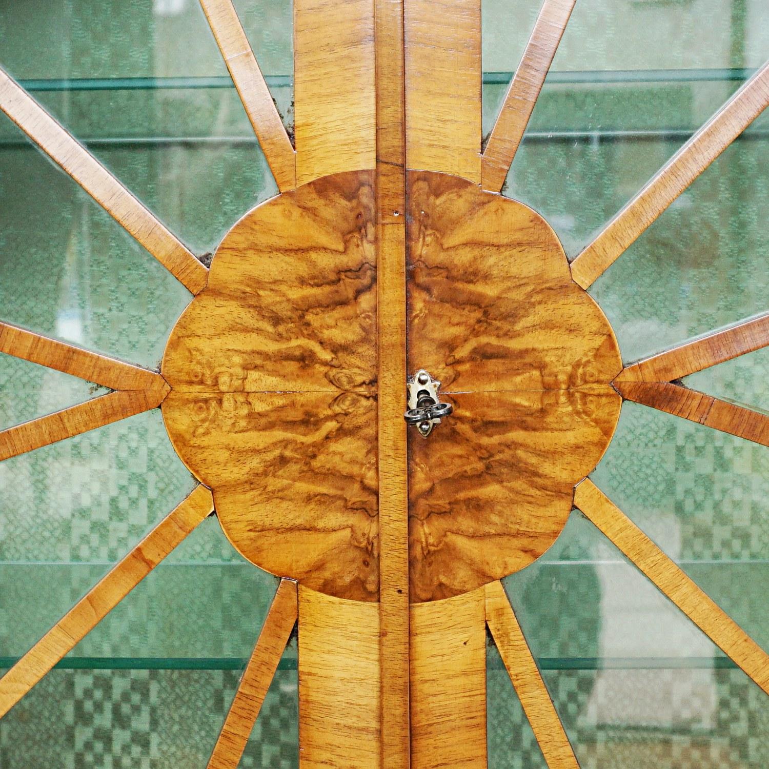 An Art Deco octagonal display cabinet. Burr walnut and figured walnut veneered with two interior glass shelves, and exterior side panelled shelving. Sunburst walnut banded and glass fronted cabinet doors. 

Dimensions: H 120.5cm W 116cm D 29.5cm