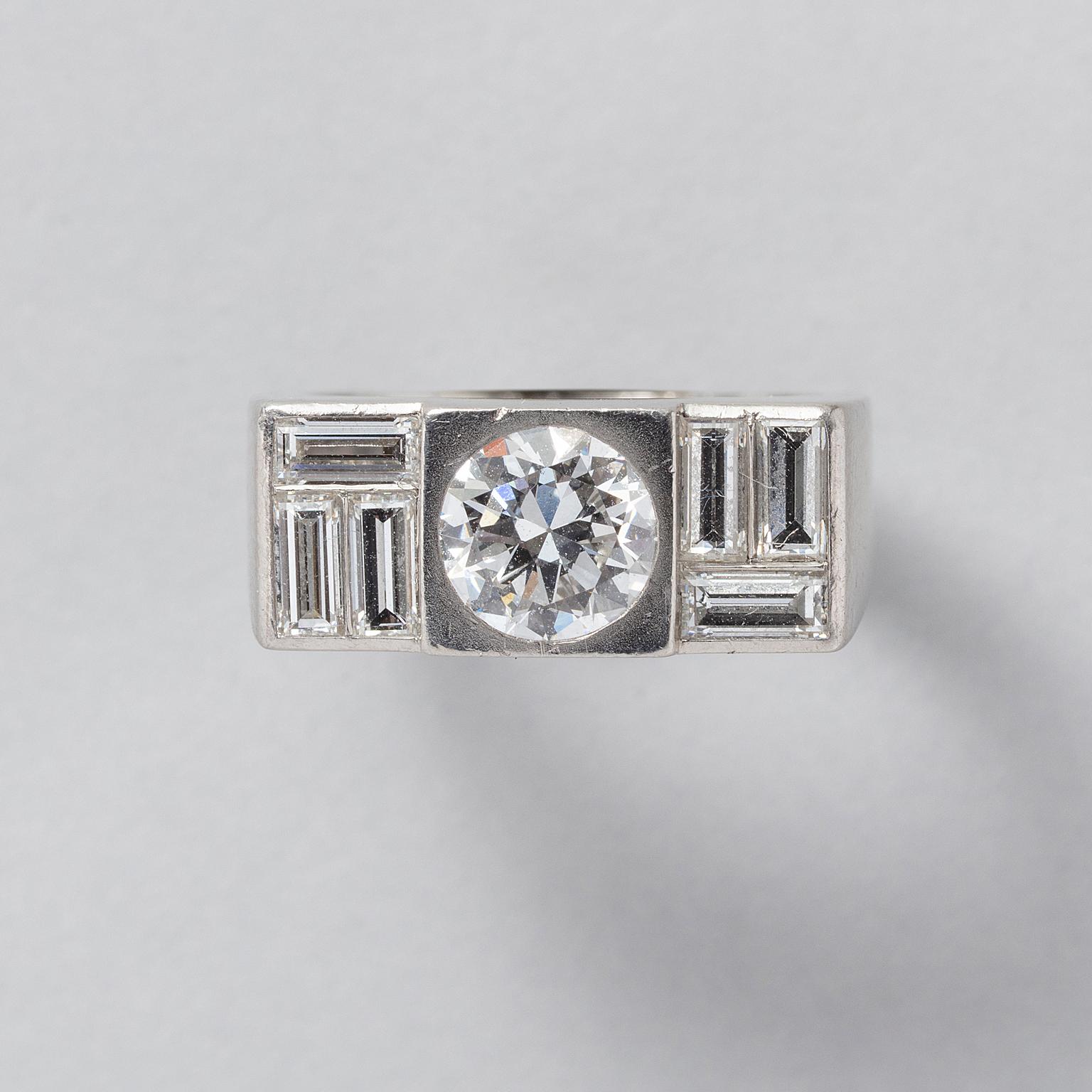 A wide platinum ring, the upper part is rectangular and tapers off in steps with a brilliant-cut diamond (app. 1.3 carats, D-E, Vs) flush set, with 6 baguette diamonds (each app. 0.15 ct E-F, Vvs and app. 2.2 ct in total HRD report no.