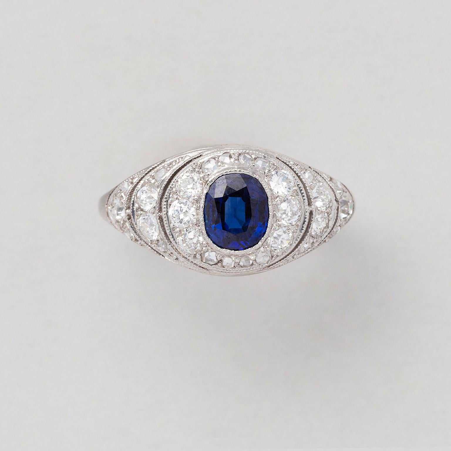 An Art Deco platinum and diamond cluster ring set with a natural unheated cushion cut sapphire (app. 1.01 carat) in the middle and brilliant cut, pavé set diamonds (app. 0.99 carat in total) all around, most likely English in origin, circa