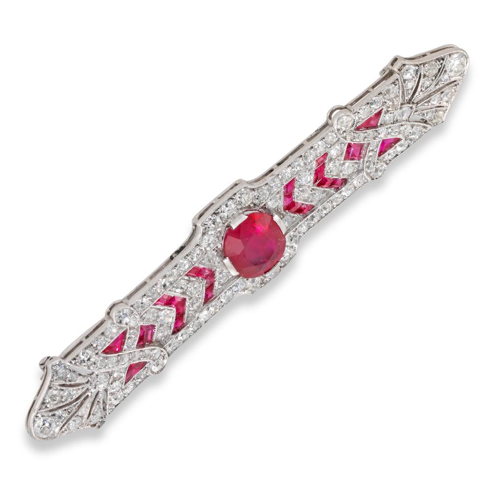 An impressive Art Deco ruby and diamond brooch, the cushion-shaped faceted ruby weighing 2.67 carats and accompanied by The Gem & Pearl Laboratory report stating to be of Burmese origin with no indication of heating, centrally-set to an elongated