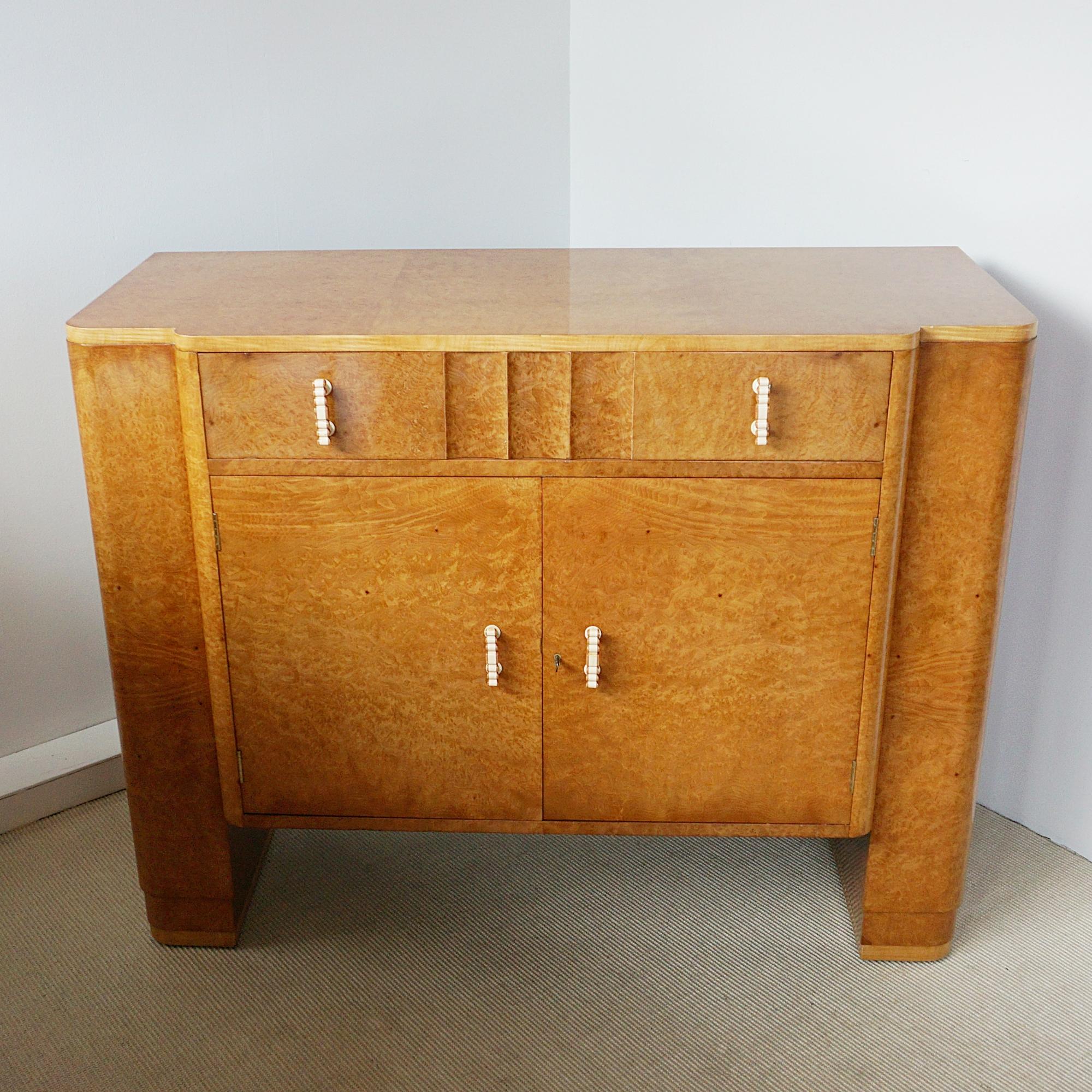 An Art Deco sideboard by Harry & Lou Epstein. Burr walnut veneered with satin wood banding on solid mahogany. Fluted upper drawer and lower cabinet section with mahogany lined shelved interior. Original bakelite handles.

Dimensions: H 96cm W 122cm