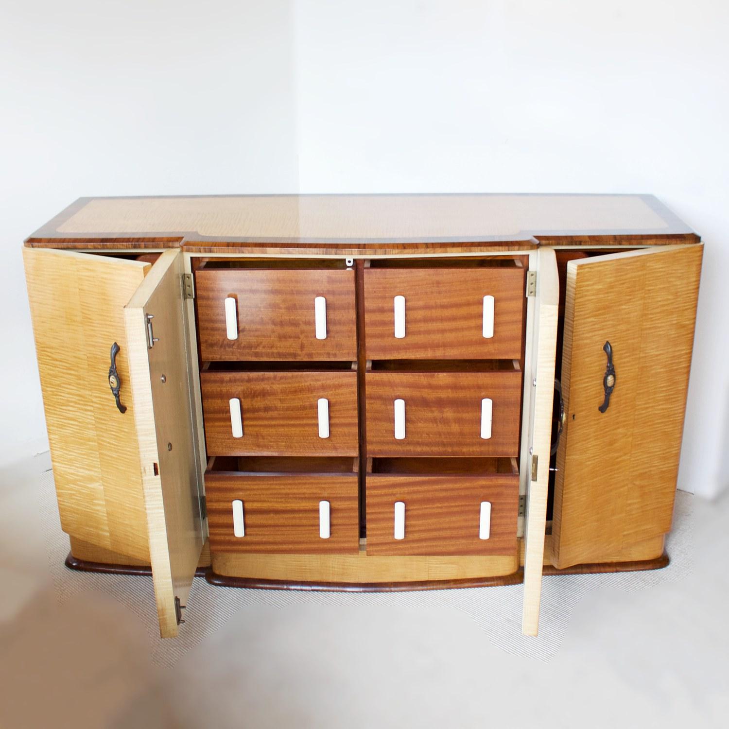 An Art Deco sideboard. Satin birch veneered with a figured walnut banding. Original metal and variegated bakelite handles to outside with white bakelite handles to interior. Six integral central drawers flanked by two shelved cupboards with upper