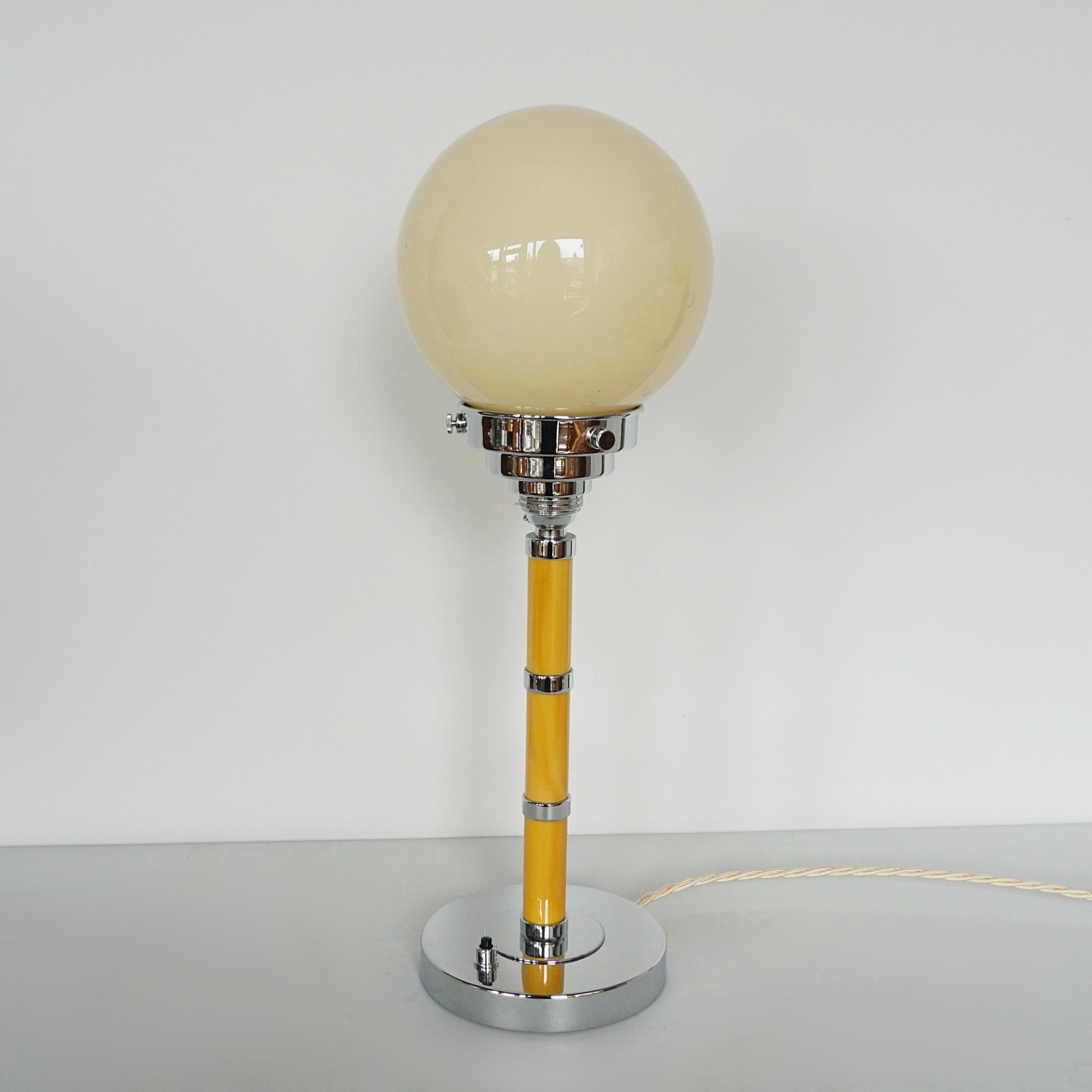 An Art Deco style table lamp. Amber bakelite stem with chromed rings and  a cream glass globe shade.

Dimensions: H 44cm W 14cm

Origin: English

Item Number: J339

All of our lighting is fully refurbished, re-wired, and re-chromed with some